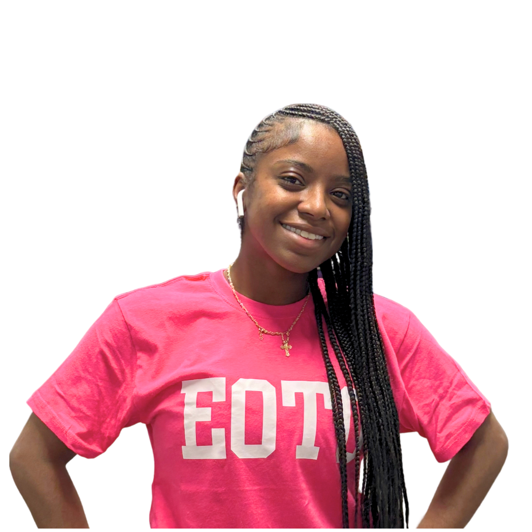 Ms. Bre'Ya Porter the Food Service Coordinator, wearing a pink T-shirt with white letters, gold necklace with a cross, and wireless earbuds, smiling confidently against a white background.