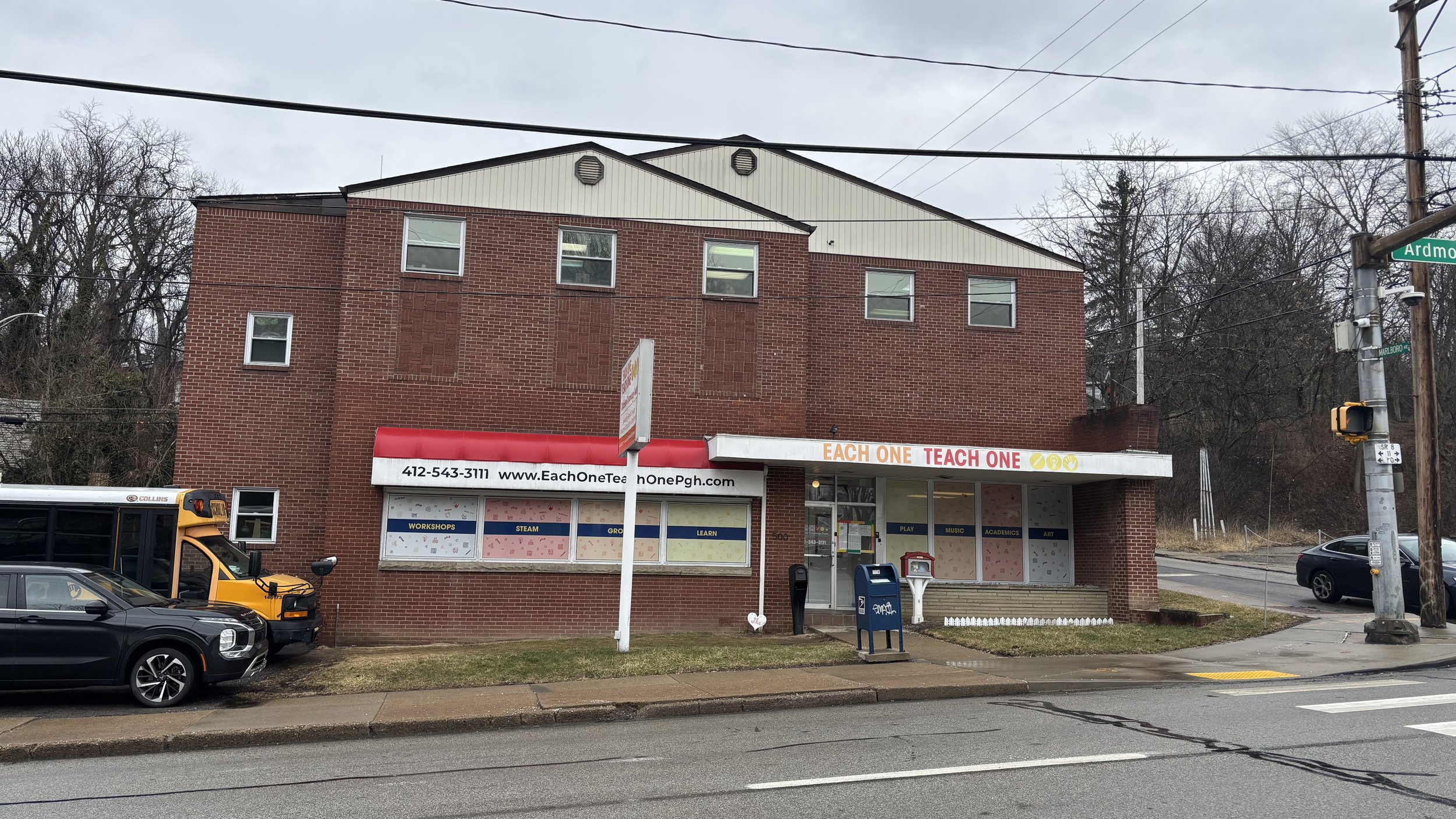 Front view of Each One Teach One Childcare & Learning Center’s Wilkinsburg location on Ardmore Blvd, featuring center signage, our yellow Each One Teach One school bus parked out front and the community library near the door.
