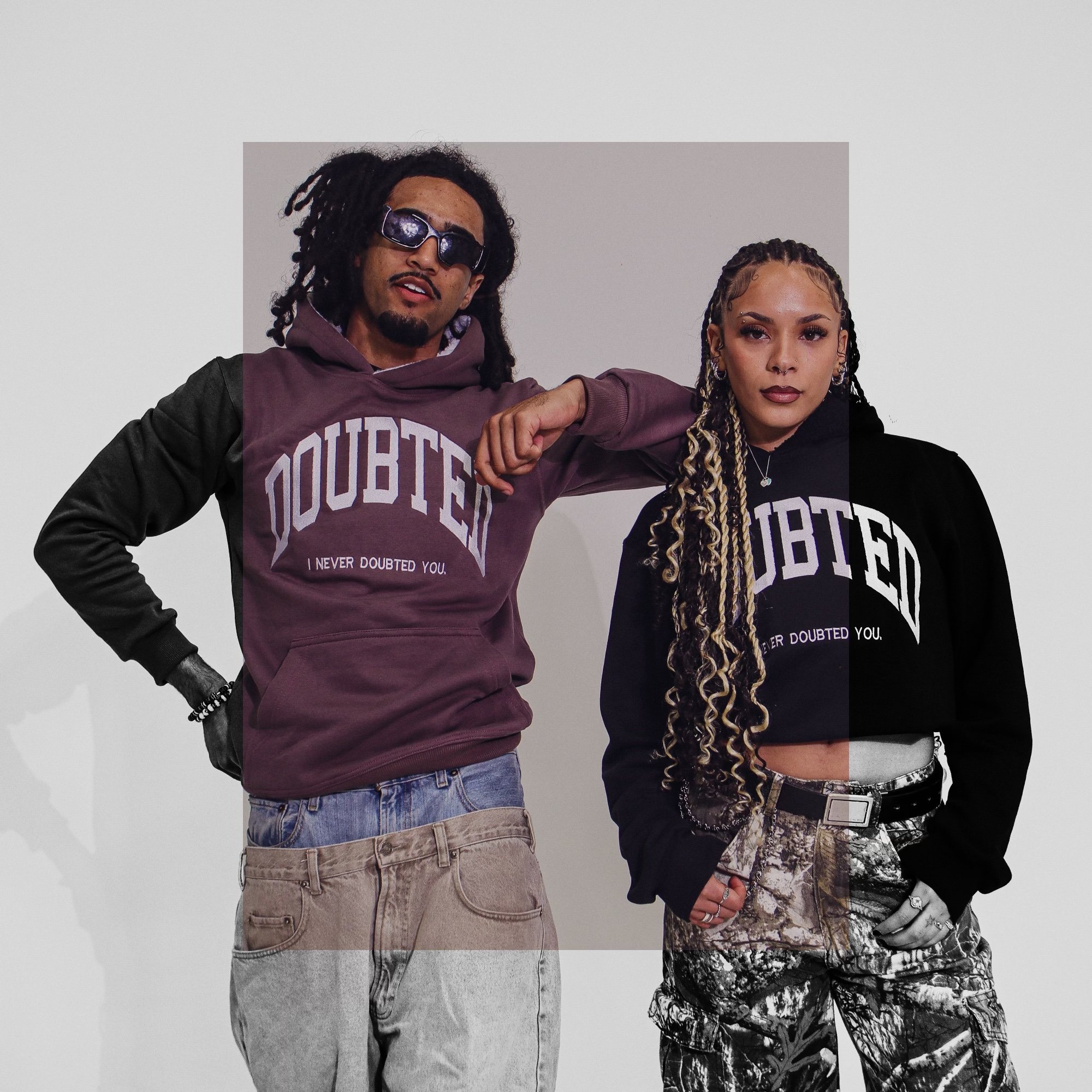 Two young adults posing together in streetwear, wearing hoodies that say 'Doubted' with the phrase 'I never doubted you,' against a plain background.