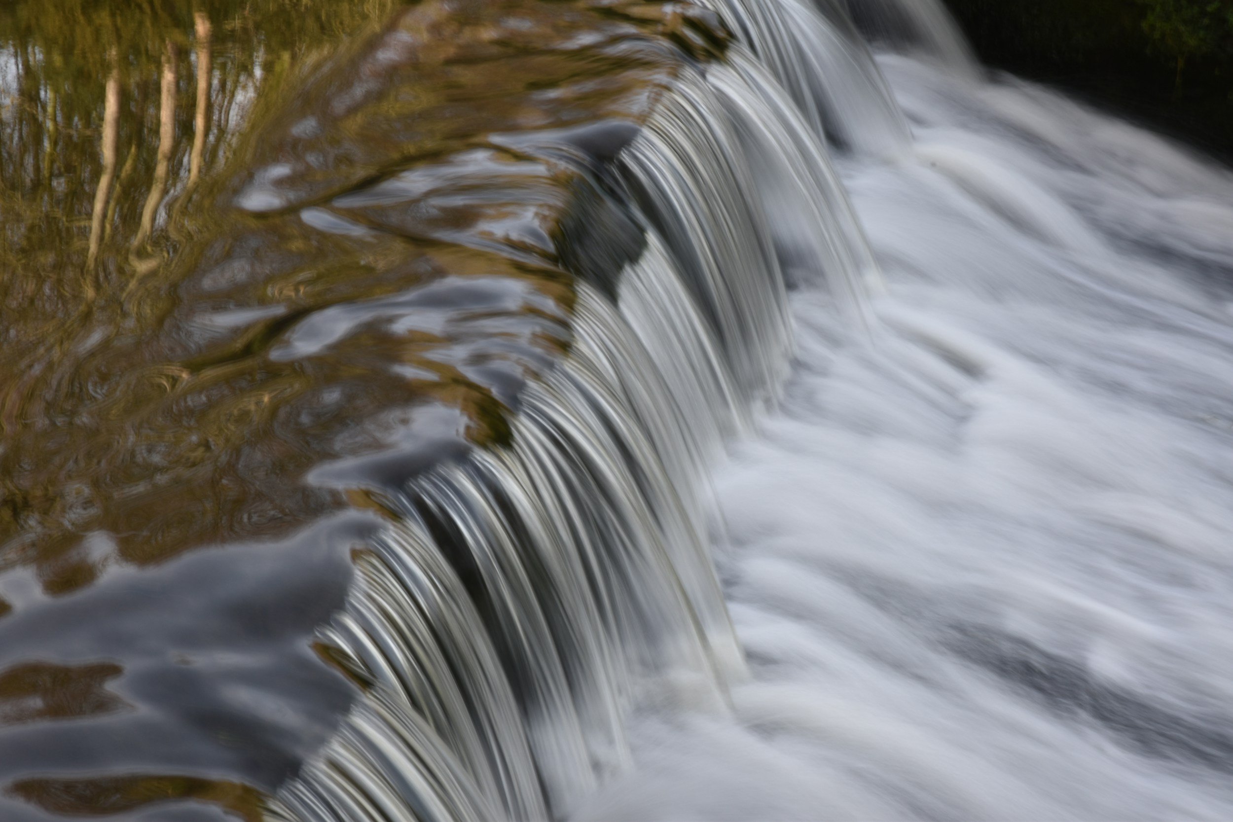 Close-up view of a small waterfall with flowing water over smooth rocks, surrounded by greenery.
