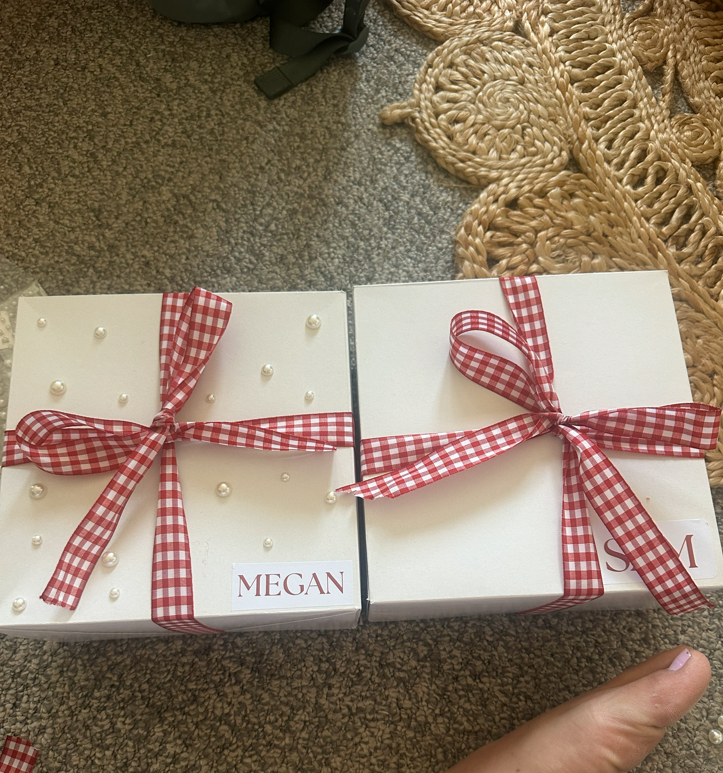 Two white gift boxes decorated with red and white checkered ribbons and small pearl embellishments, each labeled with the name 'MEGAN' and 'SAM'.