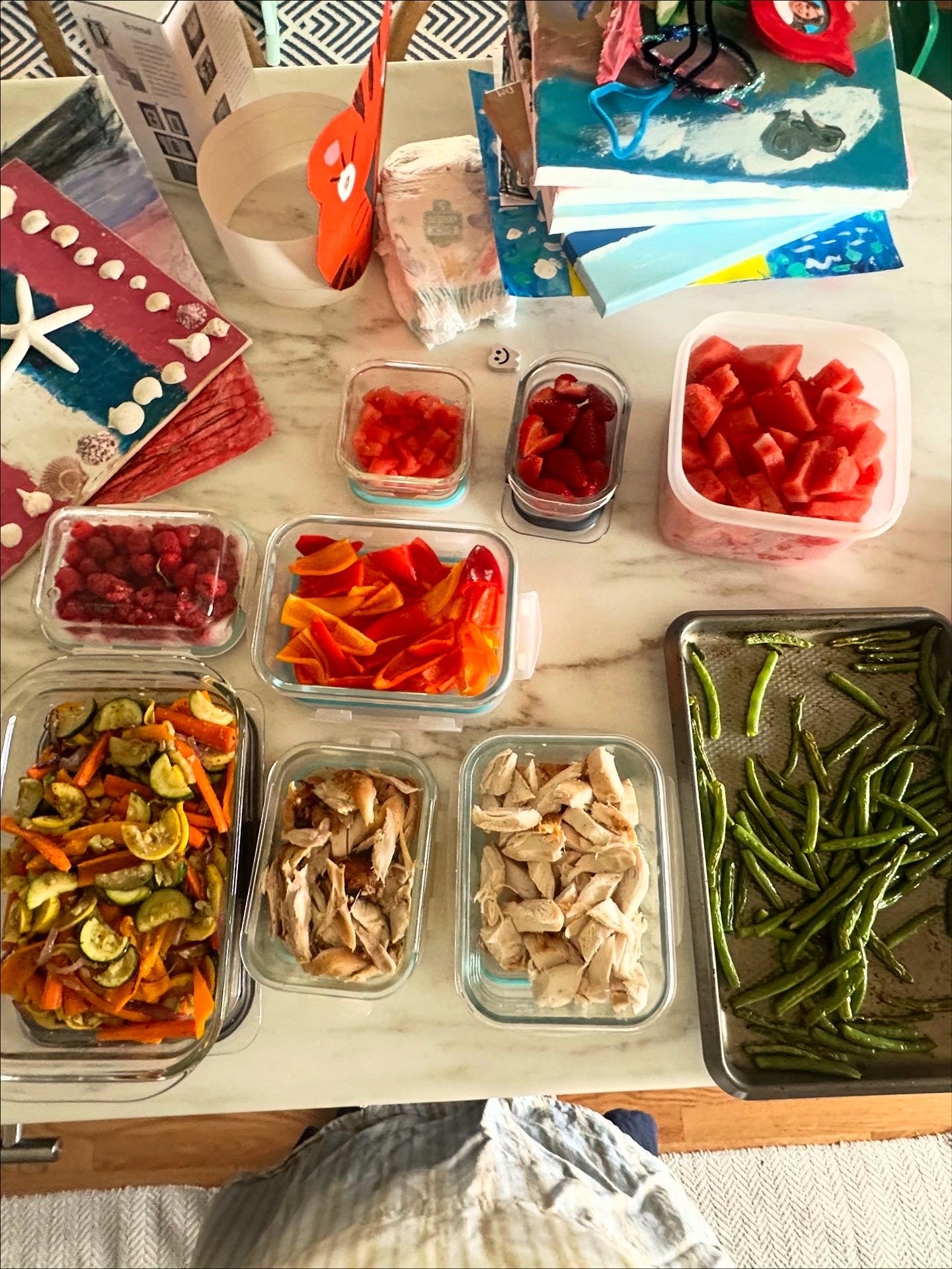 A table with various food items including cut green beans, shredded cooked chicken, sliced roasted vegetables, strawberries, watermelon, raspberries, and diced tomatoes.