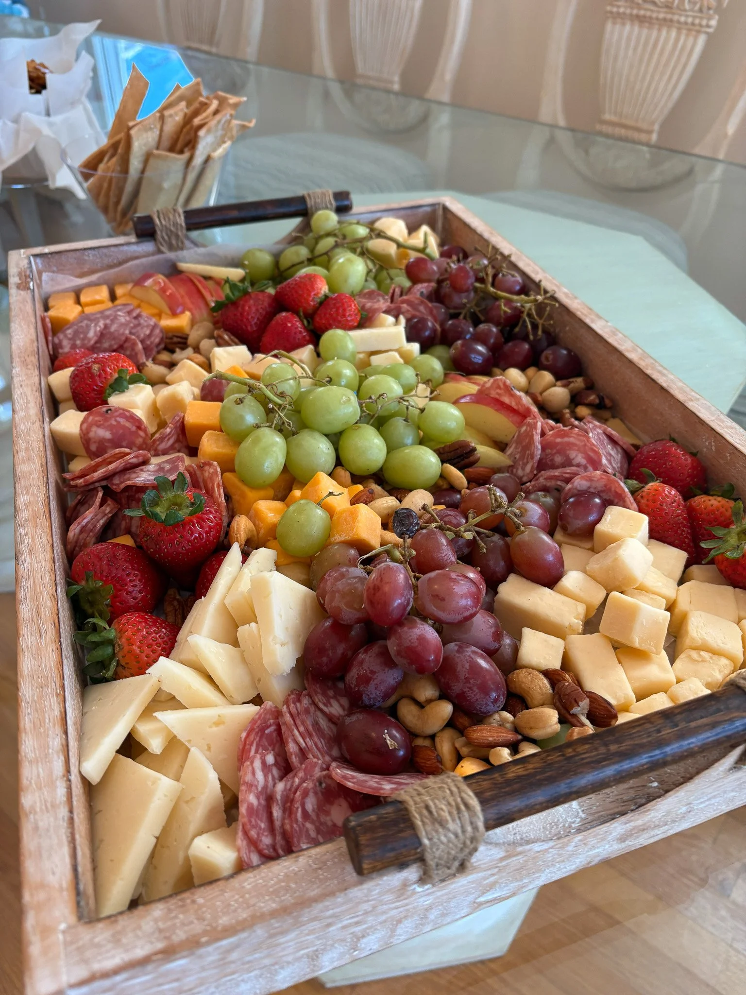 A wooden cheese and charcuterie board with grapes, strawberries, cheese, assorted meats, and nuts.