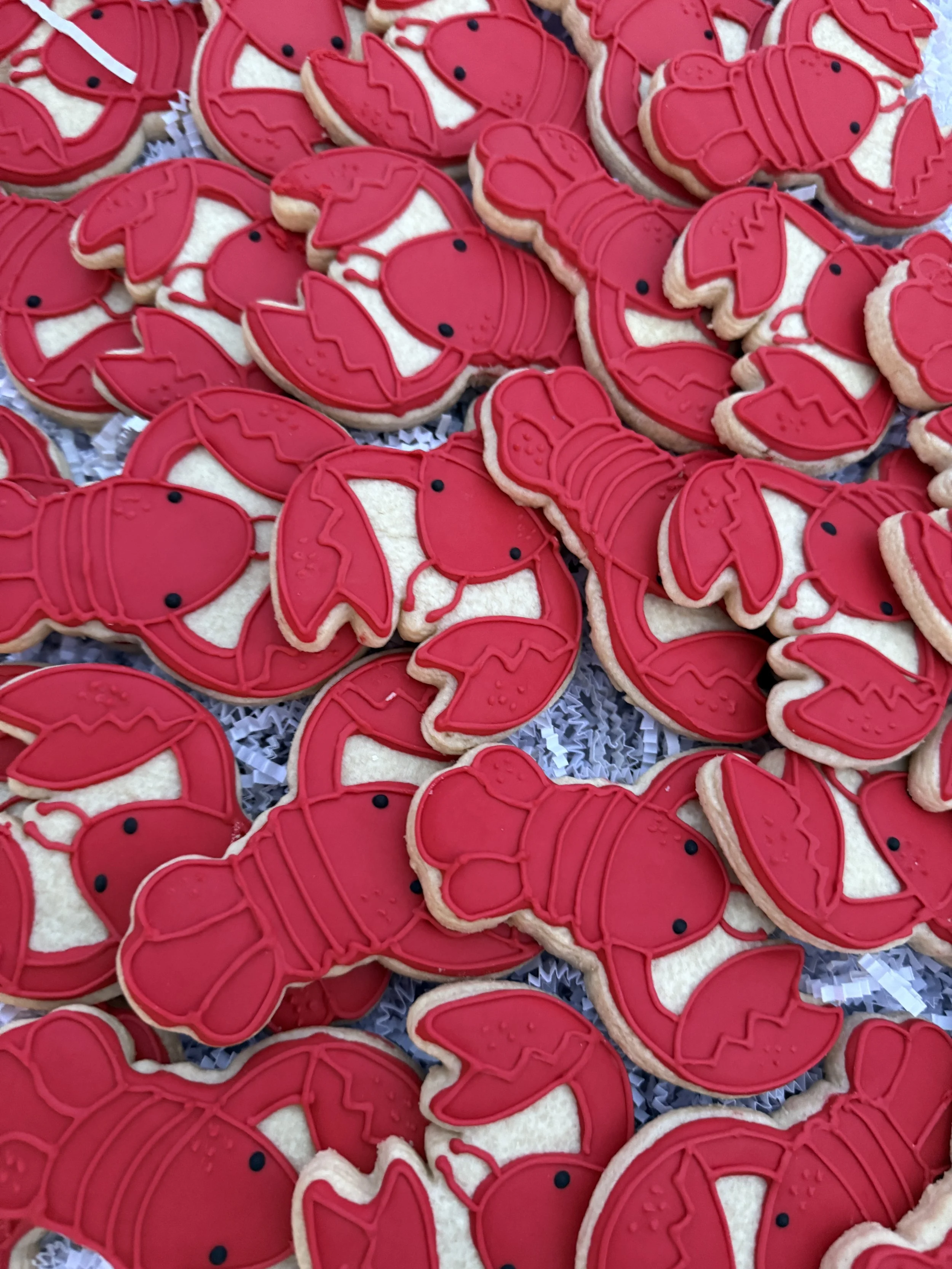 Cookies decorated as red lobsters with black eyes, arranged on a surface.