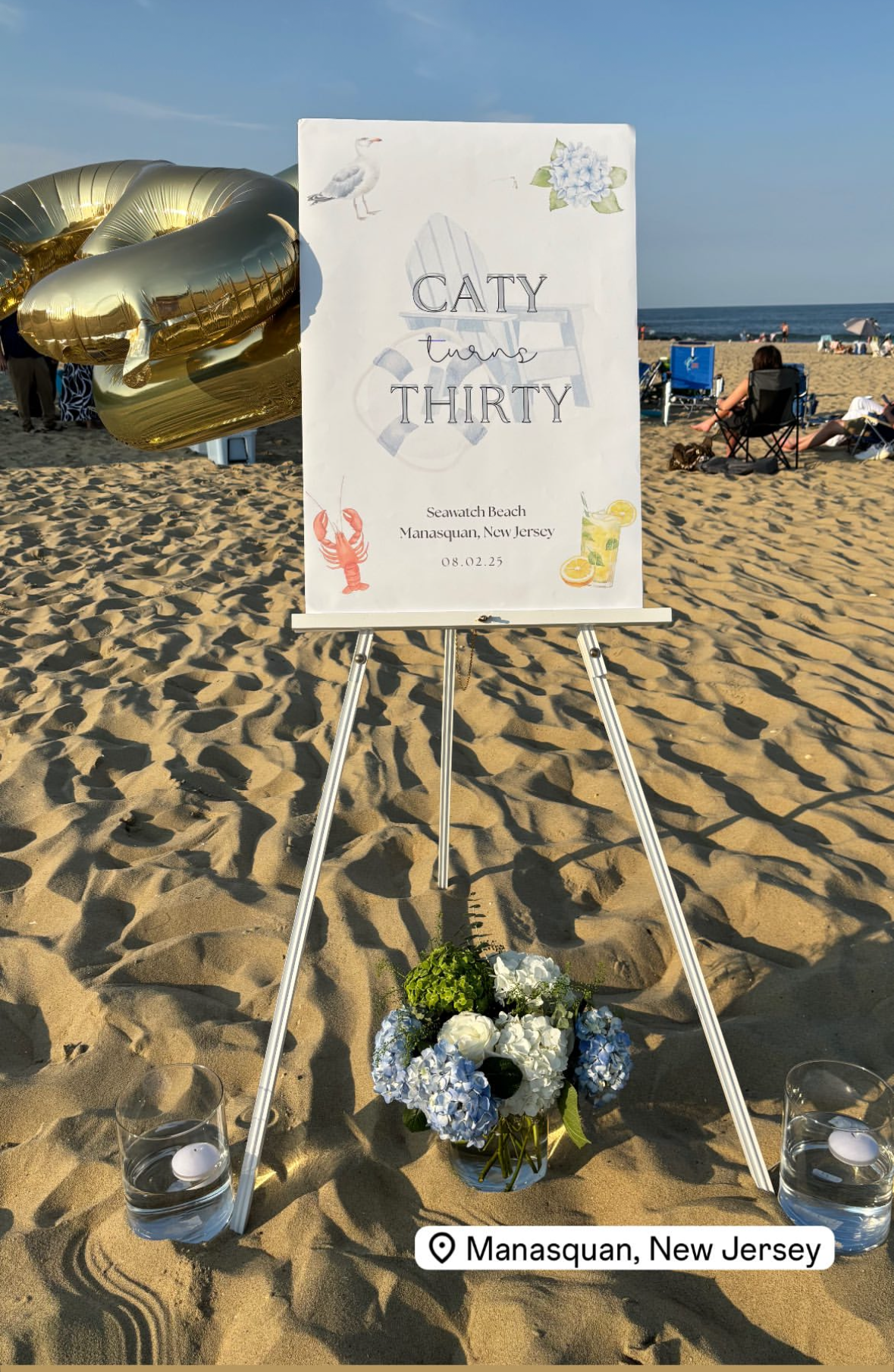 Beach wedding sign on an easel with flowers on the beach.