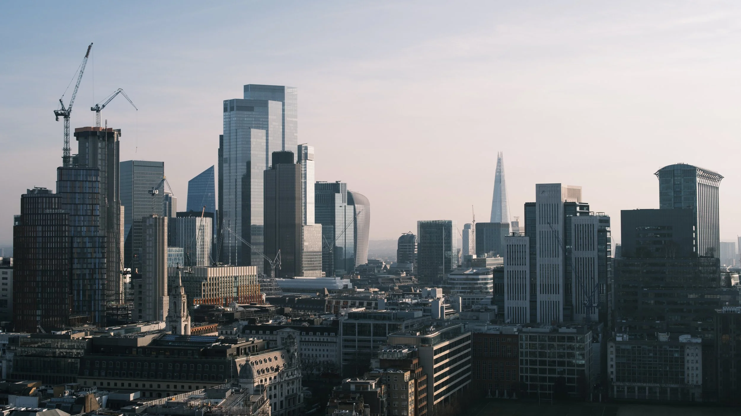 City skyline with tall skyscrapers and construction cranes under a clear sky.