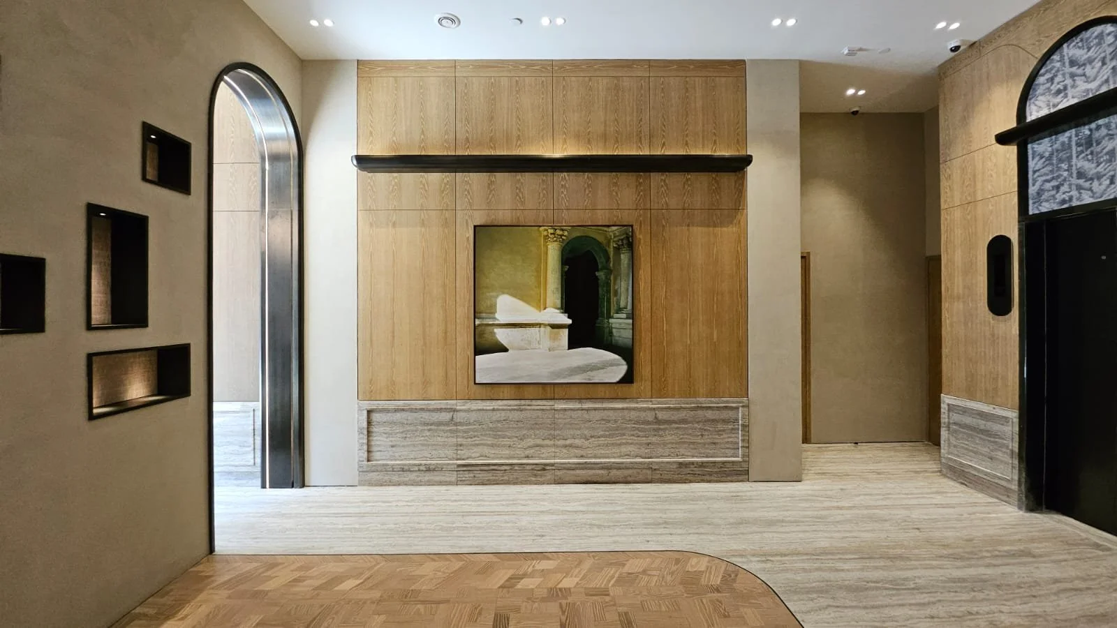 Intérieur moderne avec un mur en bois, un tableau d'art, et un passage avec porte en métal, plancher en bois, éclairage encastré.