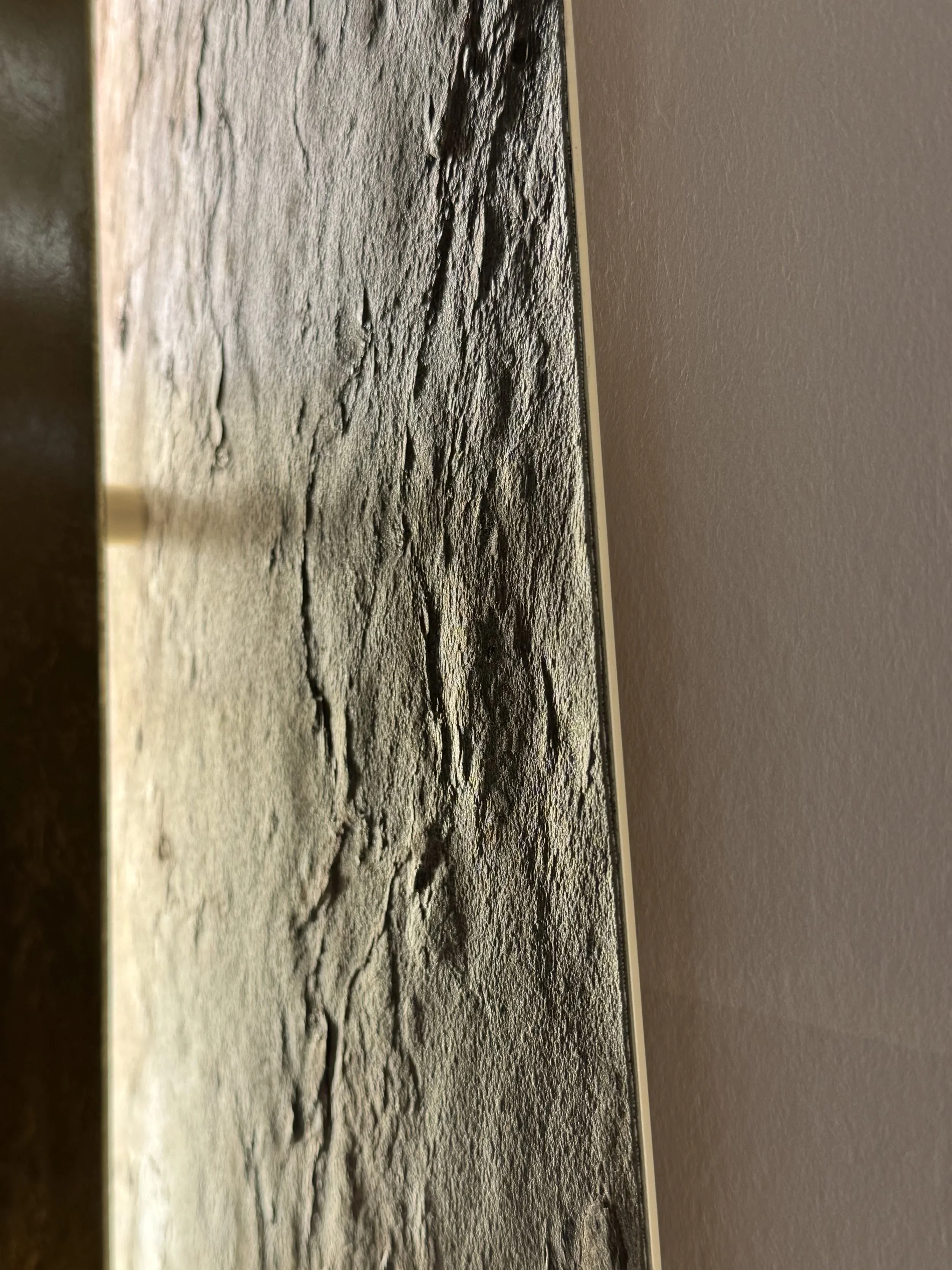 Texture rugueuse beige et grise, avec motifs de craquelures, située entre deux murs, un gris clair et un beige.