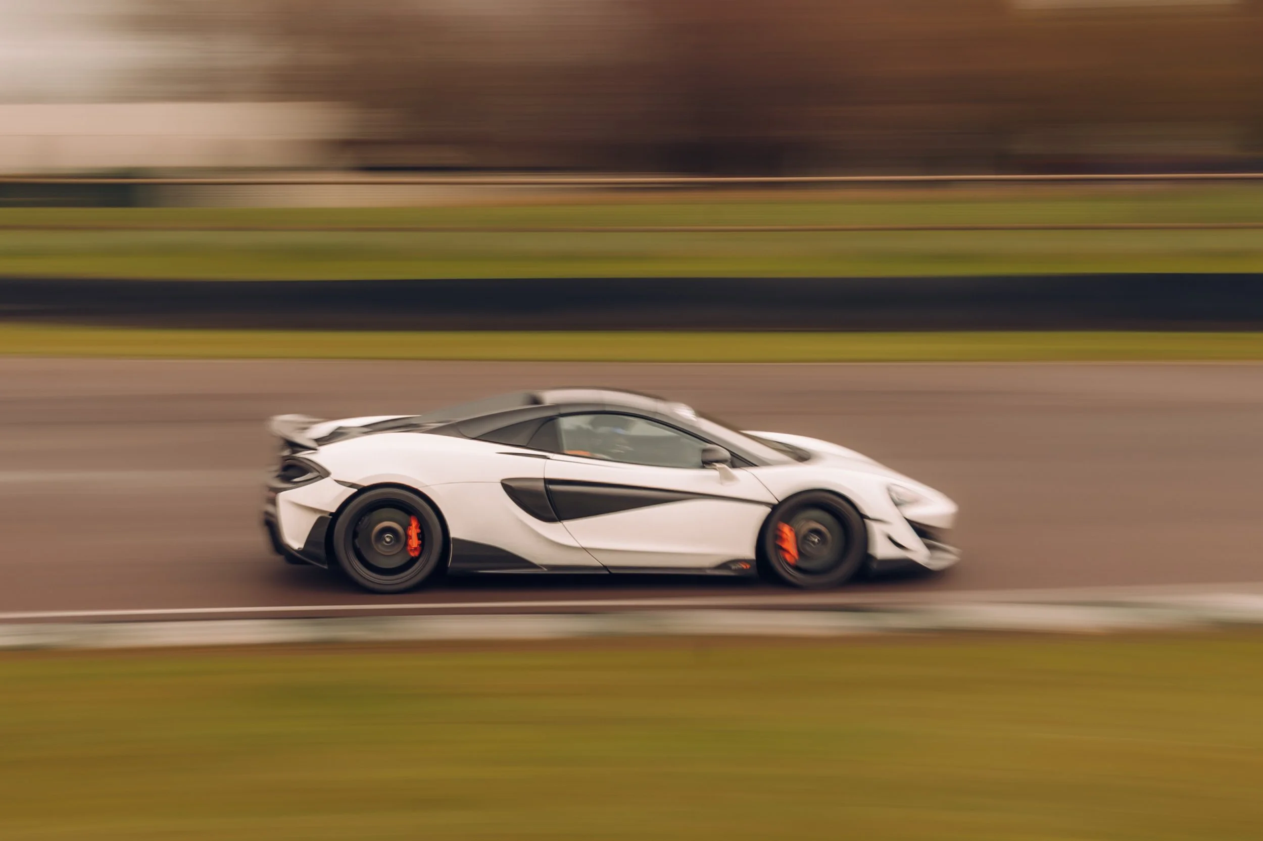 A white sports car speeding on a racetrack with a blurred background indicating motion.
