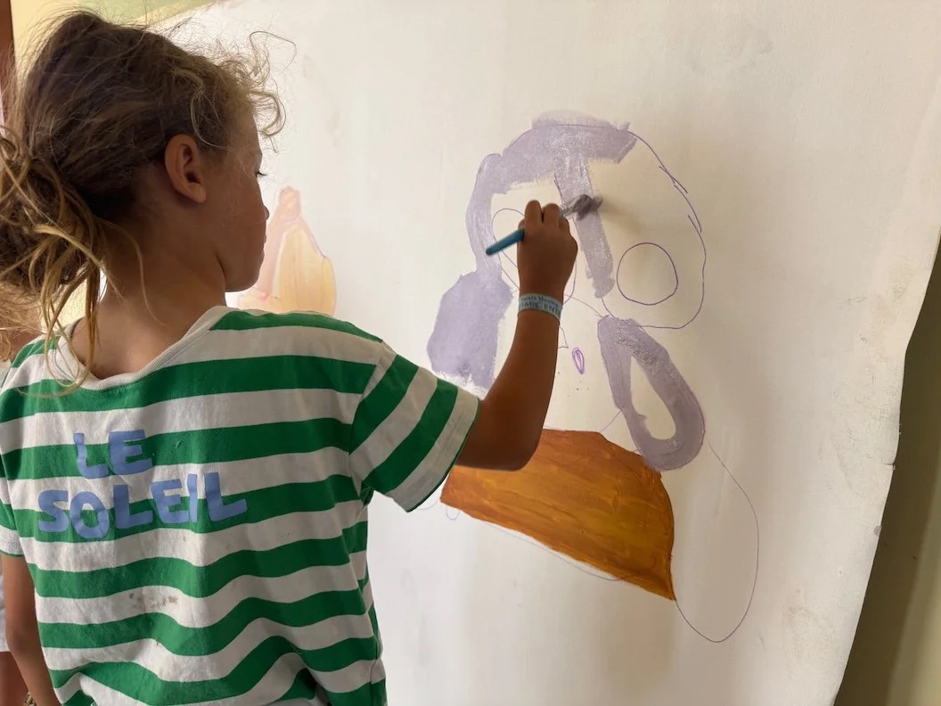 A boy in a green and white striped shirt is painting an upside-down bunny on a white wall, using purple and orange paint.