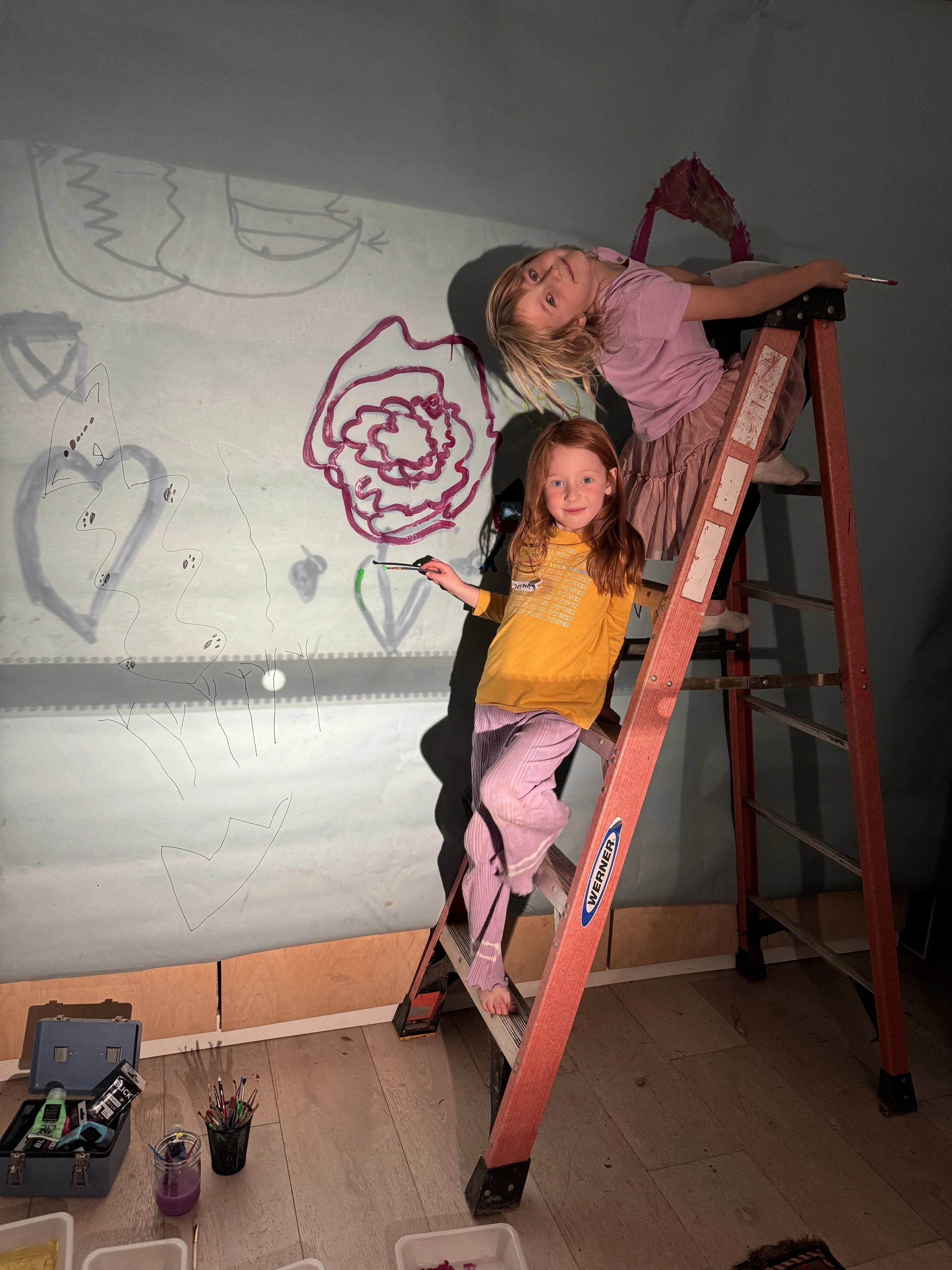 two girls on a latter tracing out their drawings being projected on the wall.