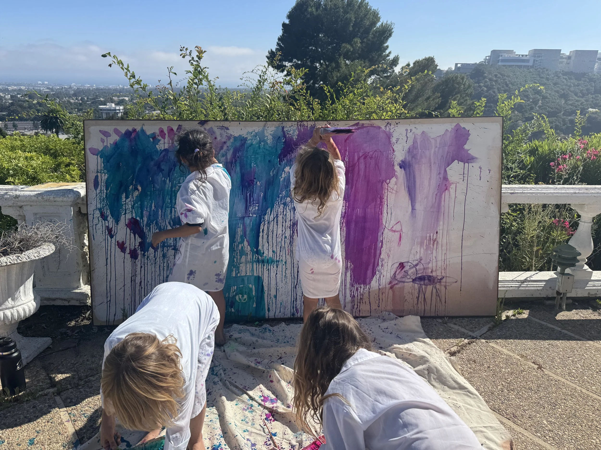 Children painting a large canvas outdoors with vibrant colors on a sunny day.