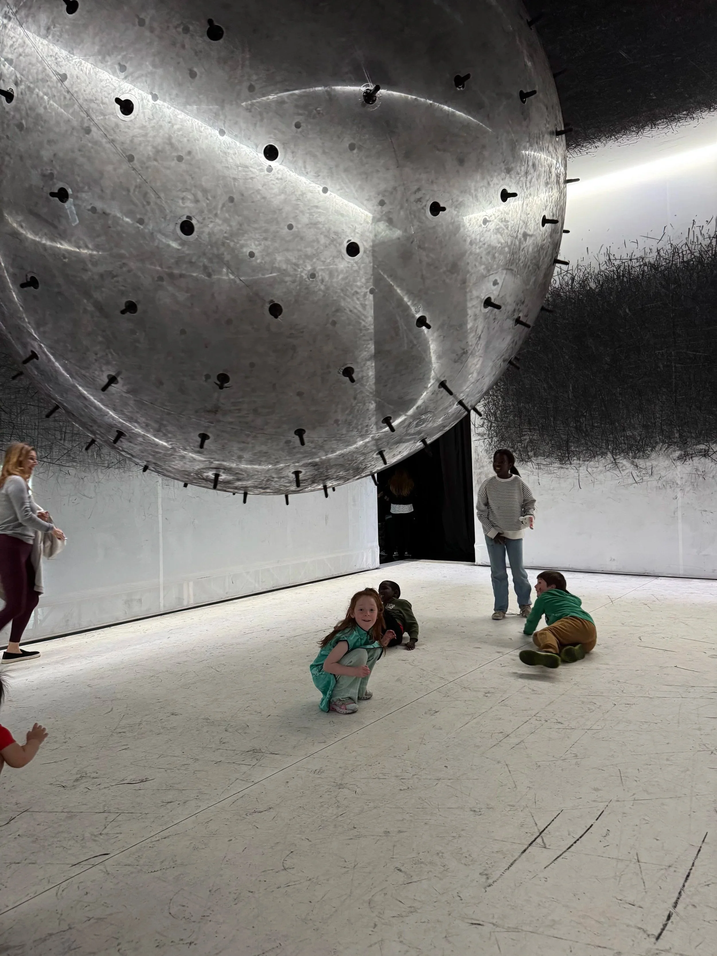girl at the balloon museum under a ball with graphite sticks attached to the outside