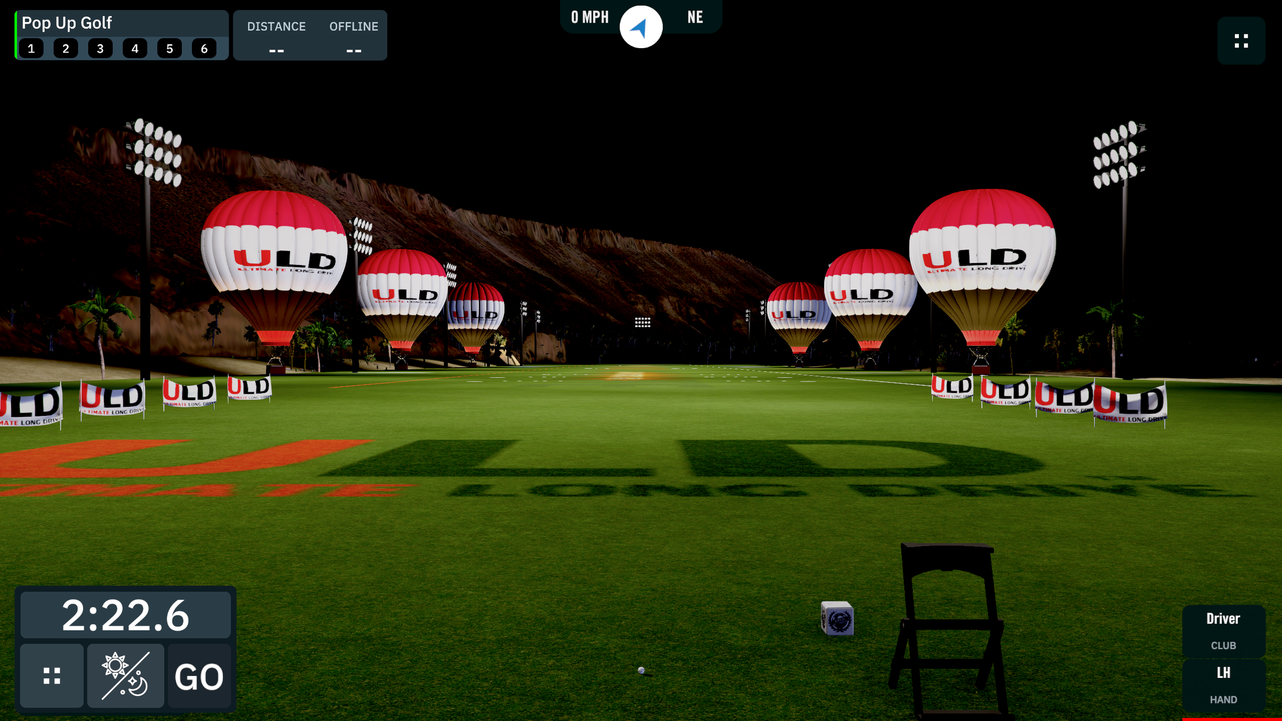 Golf driving range at night with illuminated hot air balloons displaying 'ULD' logo, surrounded by palm trees and floodlights.