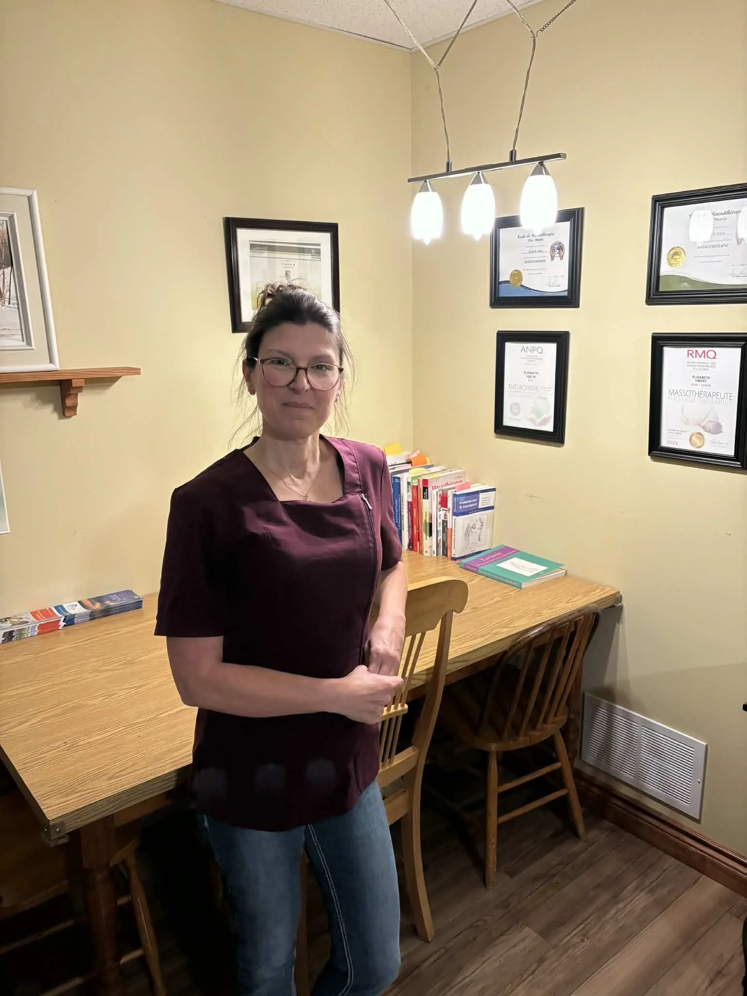 Élizabeth Vibert, massothérapeute, se tenant debout devant ses diplômes
