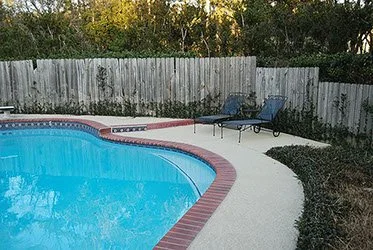 Backyard swimming pool with lounge chairs and fence in the background.