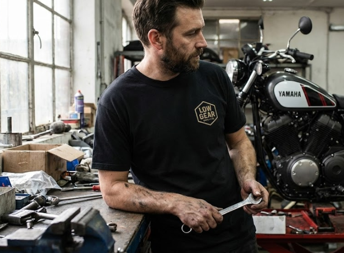A man with a beard working in a garage workshop, holding a wrench, with a Yamaha motorcycle in the background.