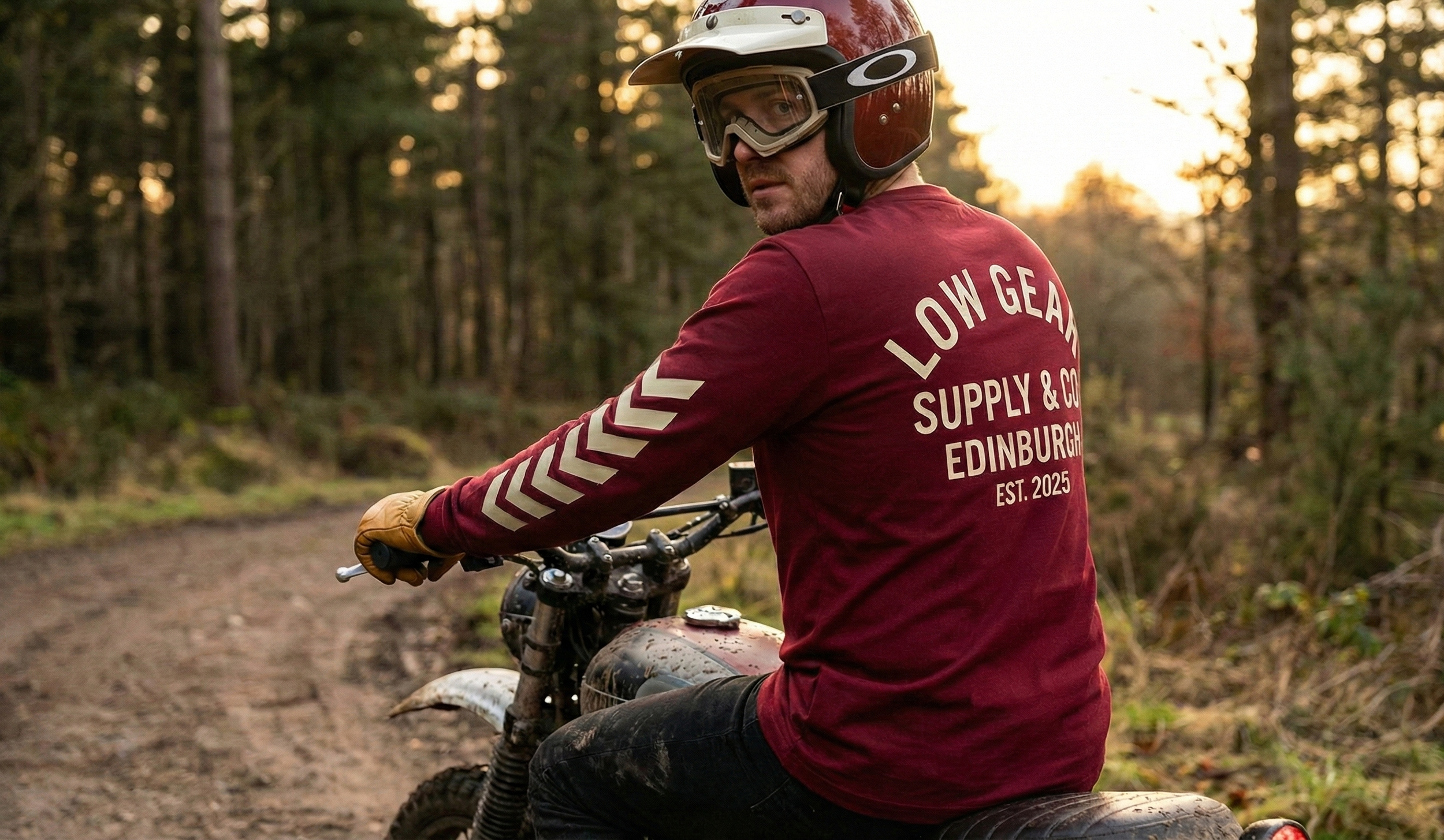 Man riding dirt bike on trail in forest during sunset, wearing helmet and gloves.