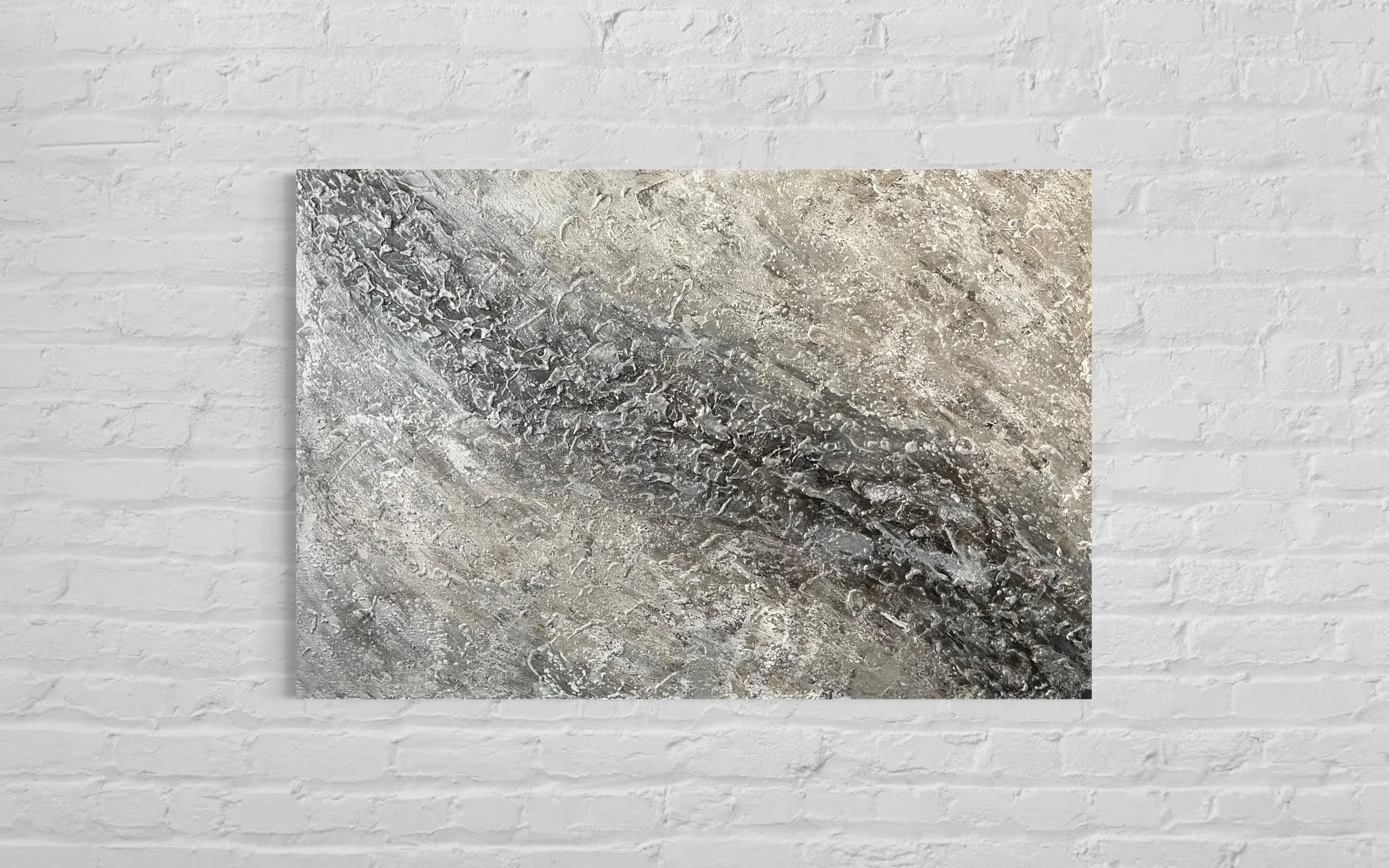 Abstract textured artwork with swirling patterns in shades of gray, beige, and black, mounted on a white brick wall.
