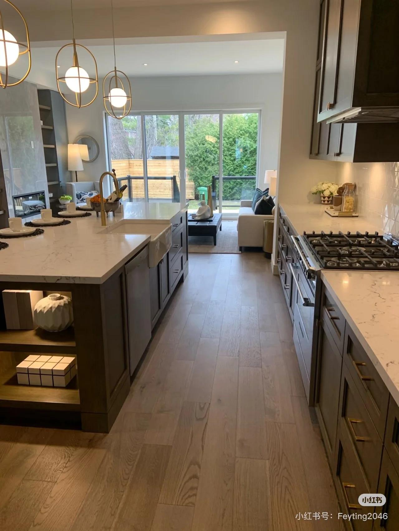 Modern open-concept kitchen and living space with white countertops, dark wood cabinets, a gas stove, and a large sliding glass door leading to an outdoor patio and greenery.