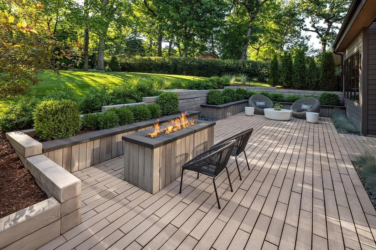 Backyard patio with a fire feature, black chairs, and modern patio furniture, surrounded by landscaped greenery and trees.