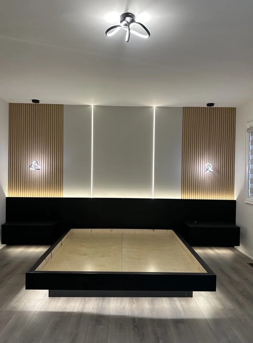 Modern living room with black built-in seating, minimalist decor, wood paneling on wall with vertical slats, LED strip lighting, and a ceiling fan with unique blades.