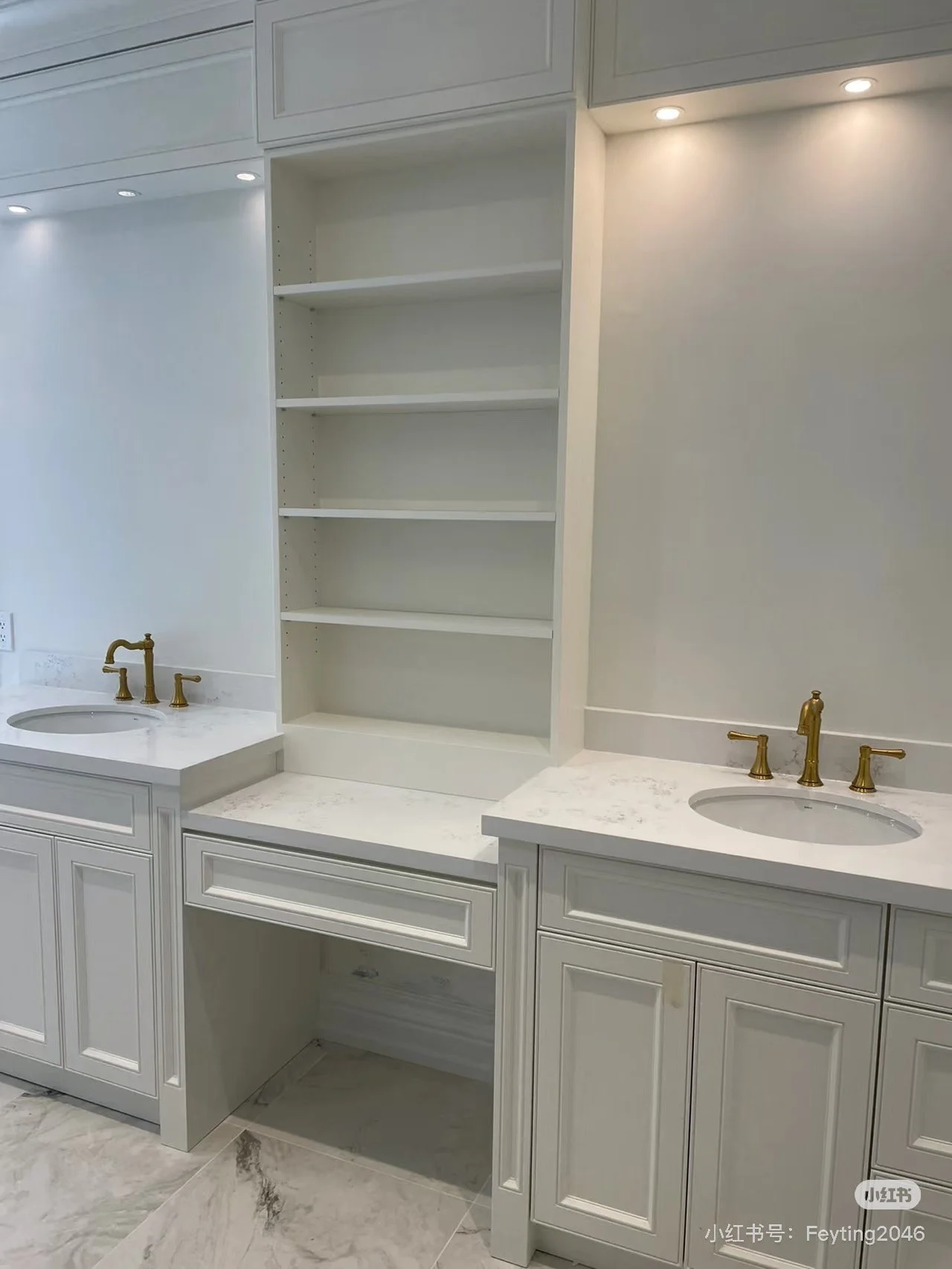 Bathroom vanity with two sinks, gold faucets, white cabinets, marble countertops, and open shelving in the center.