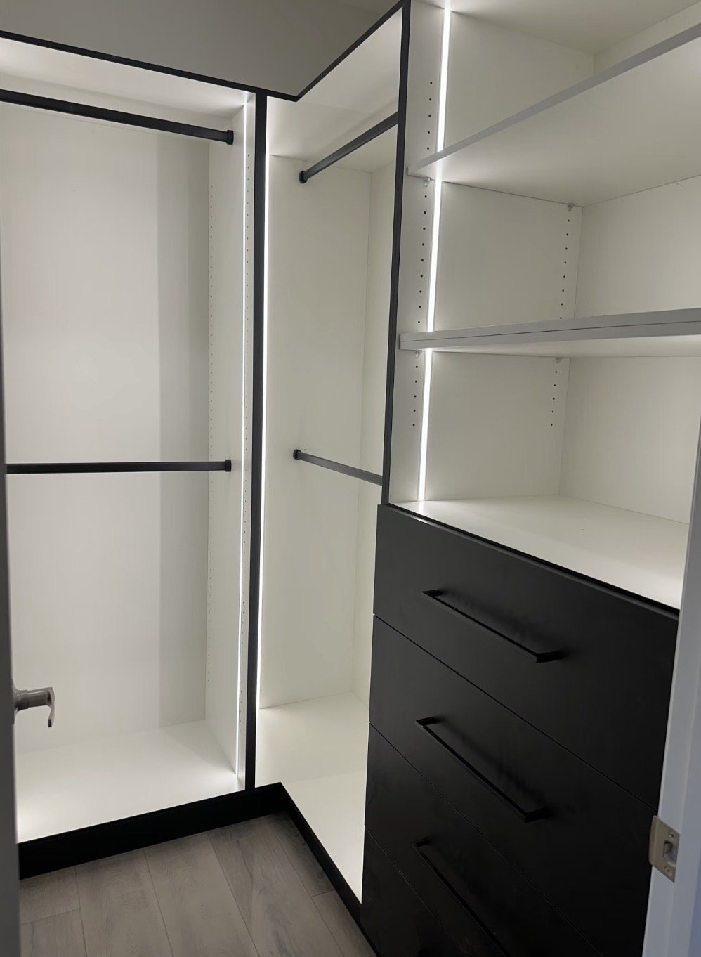 Empty walk-in closet with white shelving, black hanging rods, and black drawers.