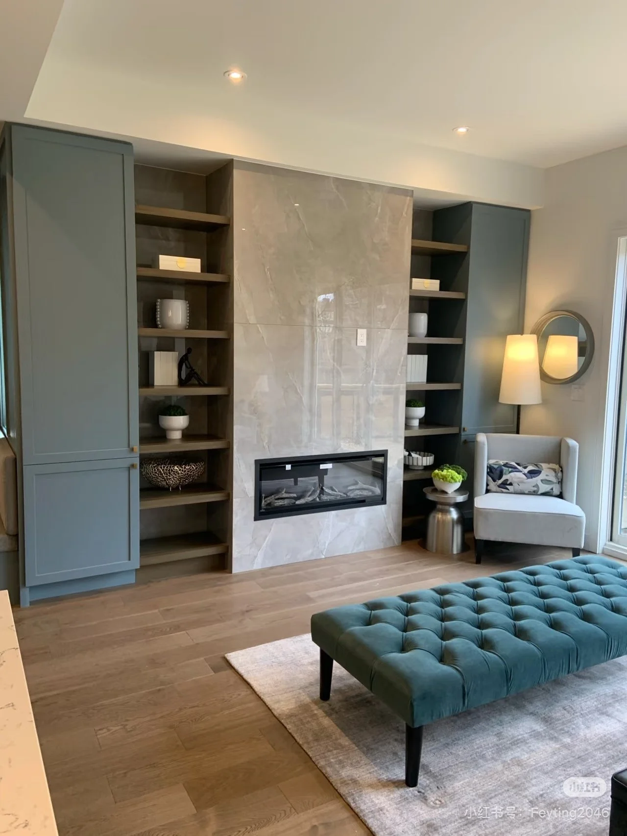 Living room with built-in shelves, a marble fireplace, a blue upholstered bench, and a white armchair with a pillow.