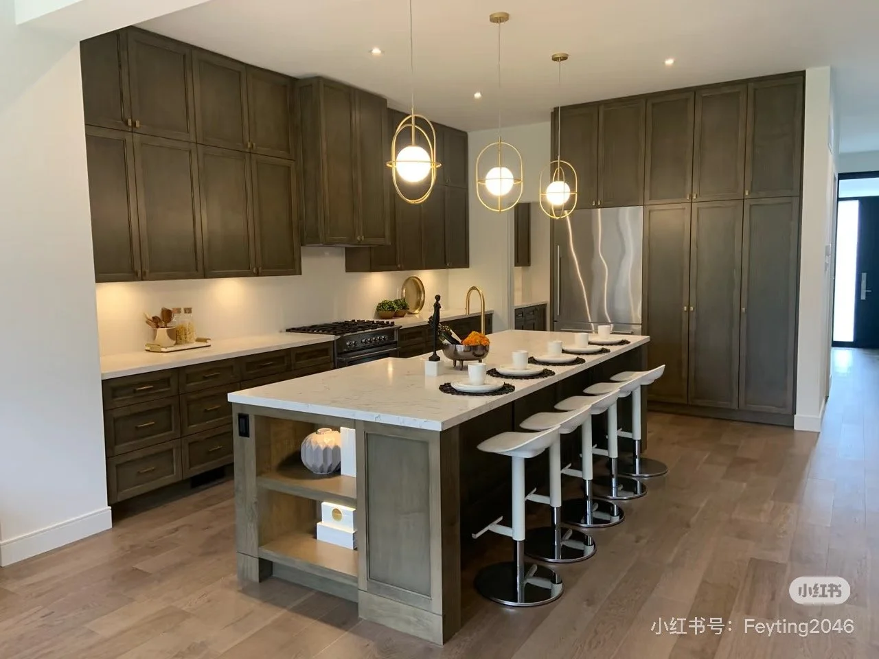 Modern kitchen with wooden cabinets, a white marble island with white barstools, pendant lights, and stainless steel refrigerator.