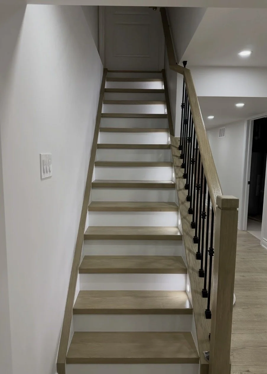 Interior staircase with light wood steps and black metal balusters, leading to the upper floor in a modern home.