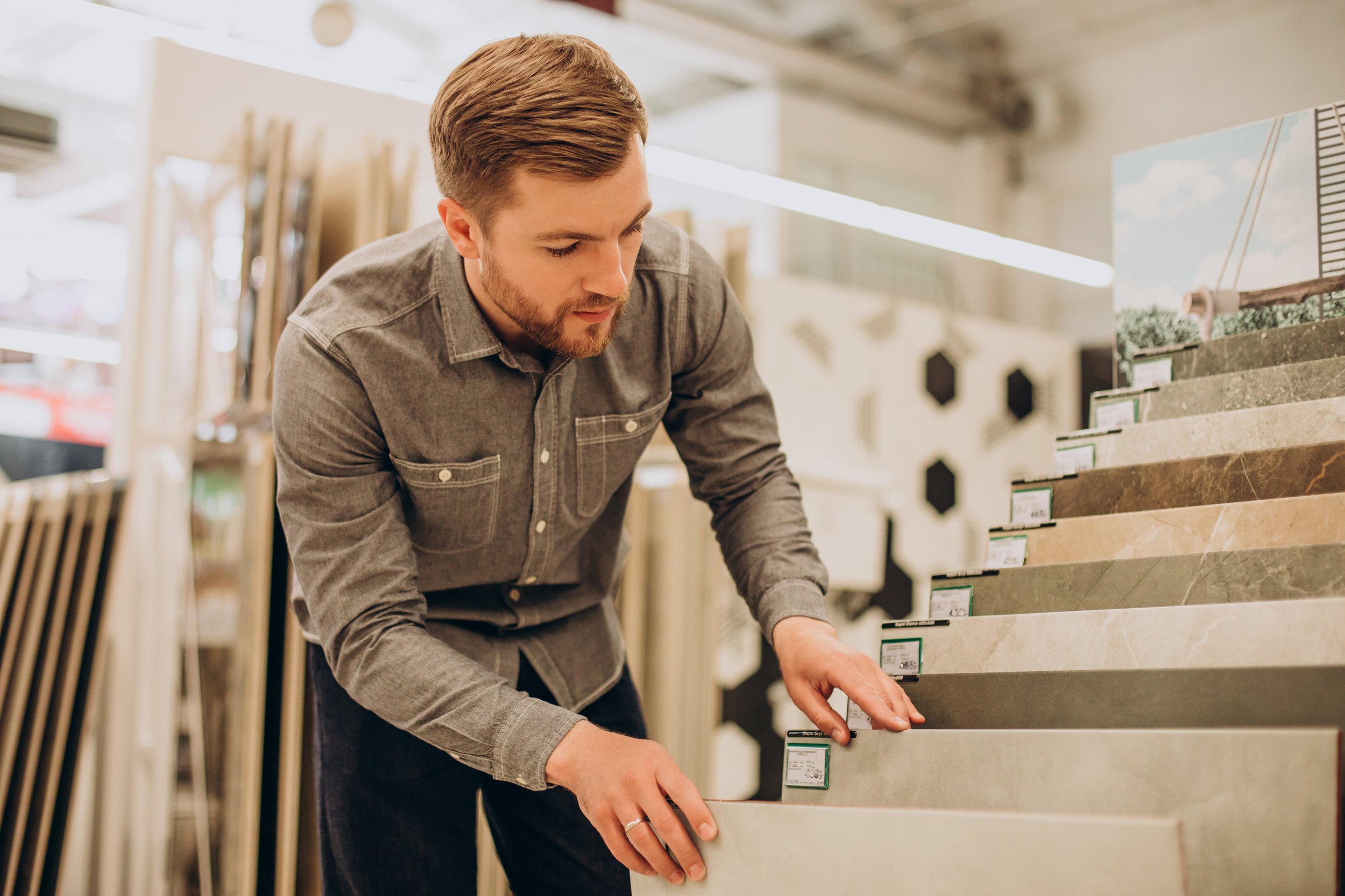 A man browsing various colors and patterns of tiles in a store, examining and selecting a tile.