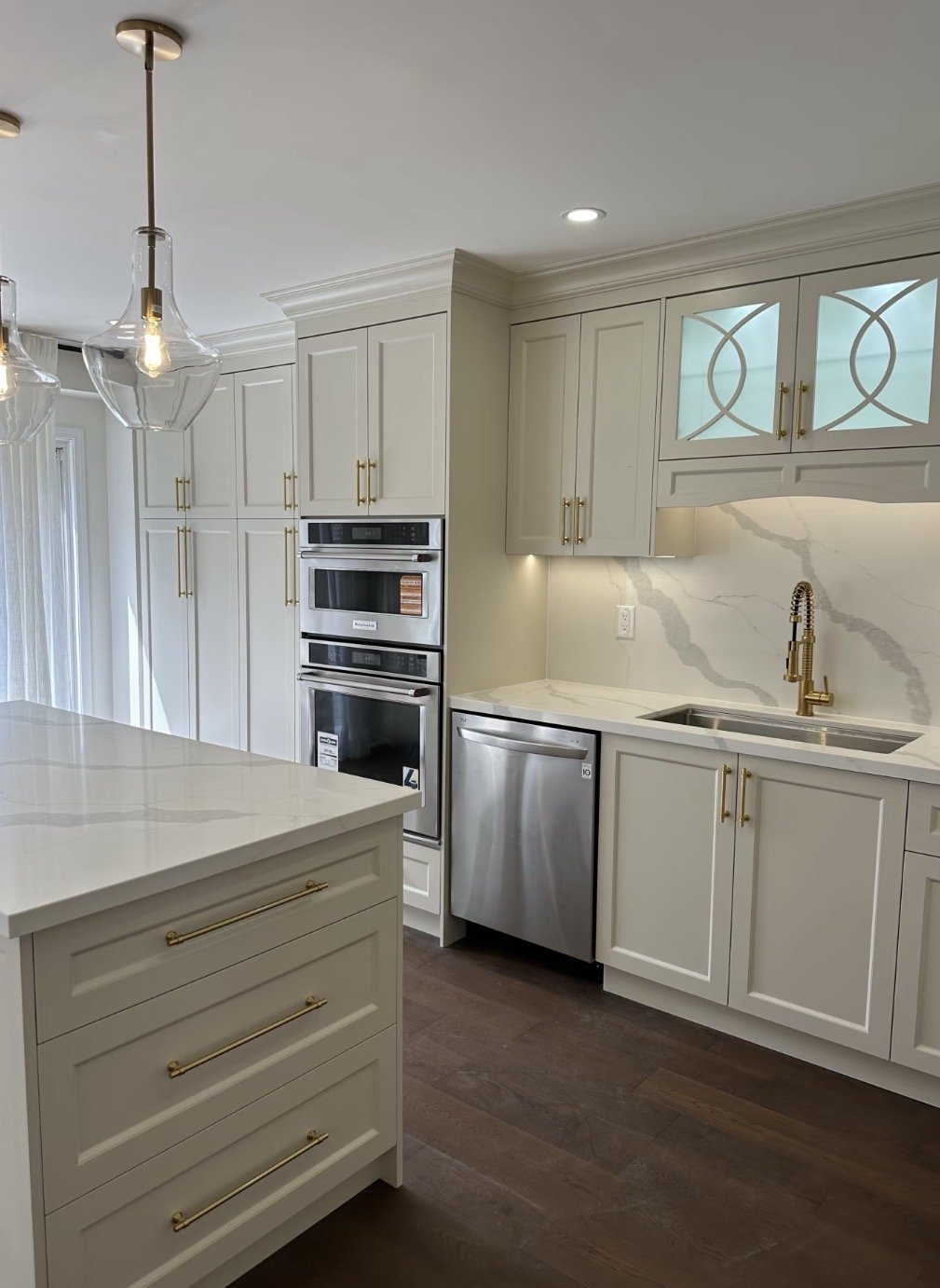 Modern kitchen with white cabinets, marble backsplash, stainless steel appliances, gold hardware, dark hardwood flooring, pendant lights.