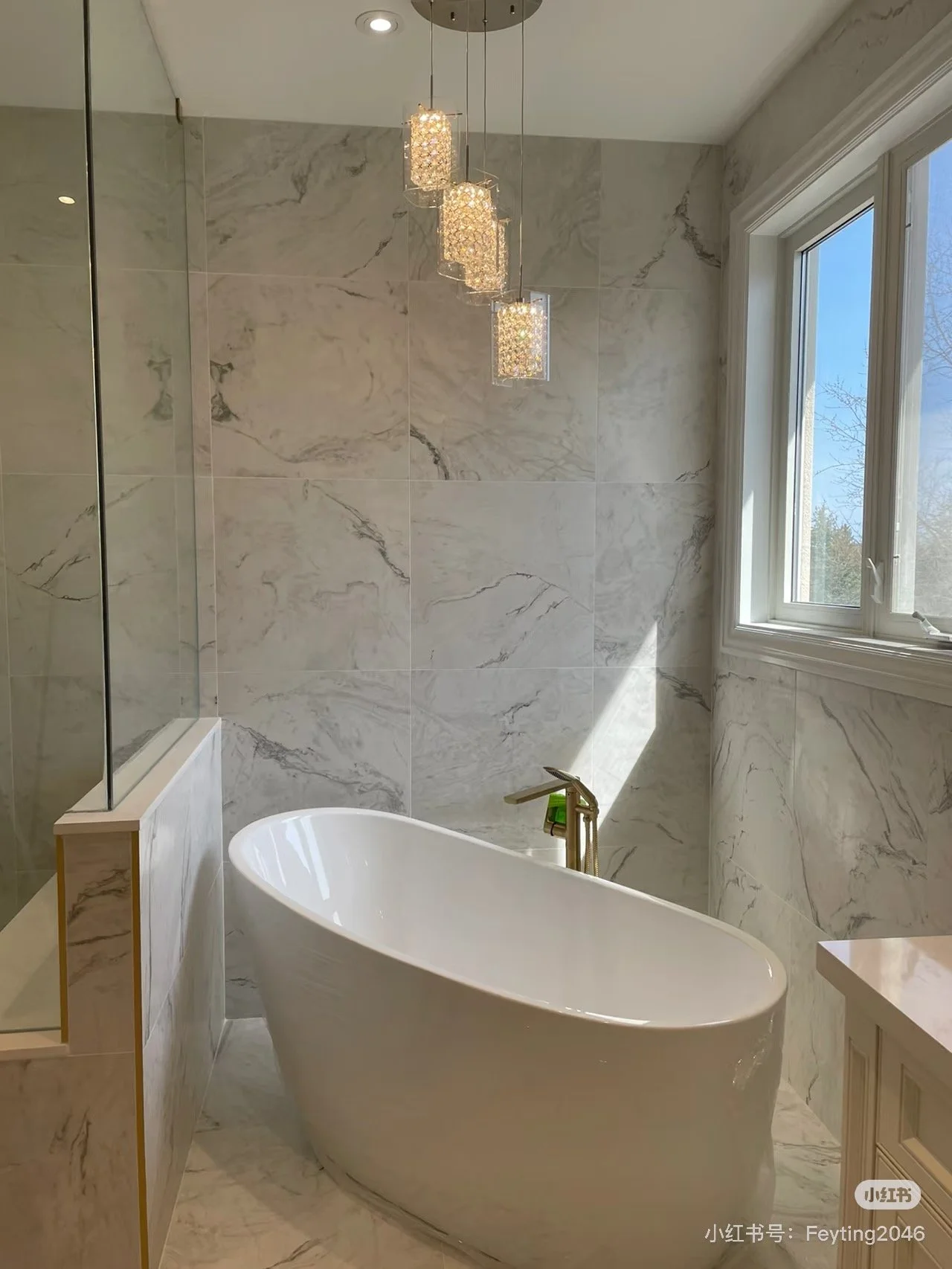 A bathroom with a freestanding bathtub near a window, marble walls, and hanging pendant lights.