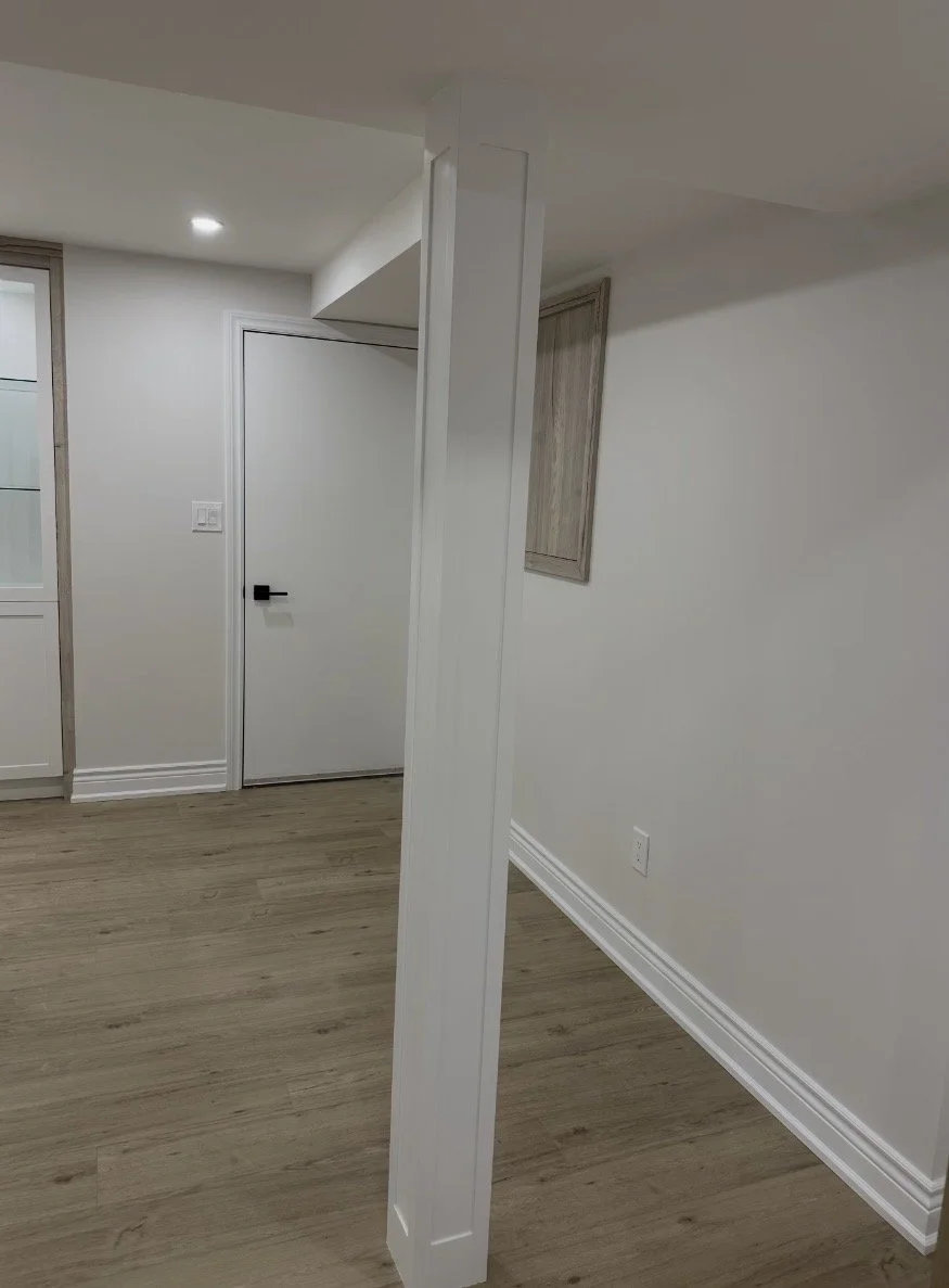 Empty room with white walls, hardwood floor, white door with black handle, glass-front cabinet, and some wooden cabinetry on the wall.