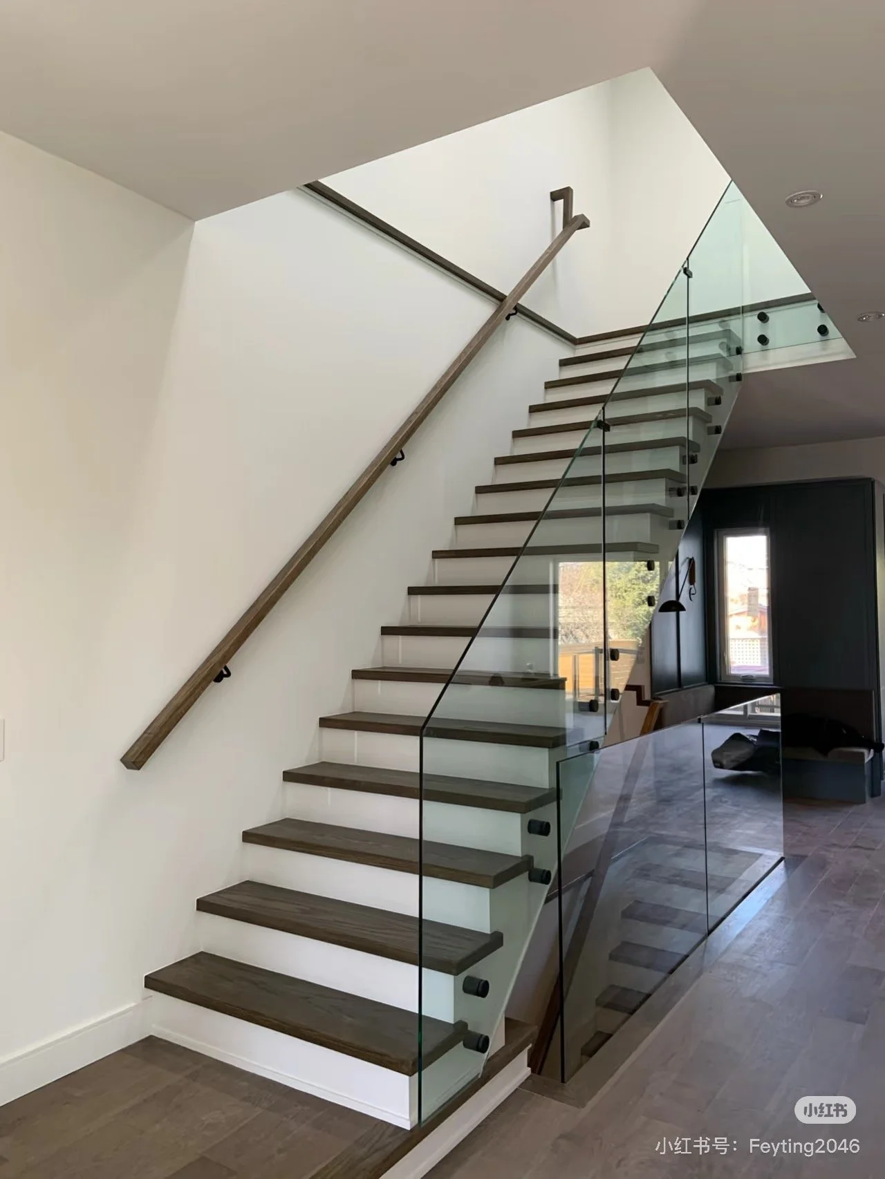Modern staircase with dark wood steps and glass railing in a contemporary home.