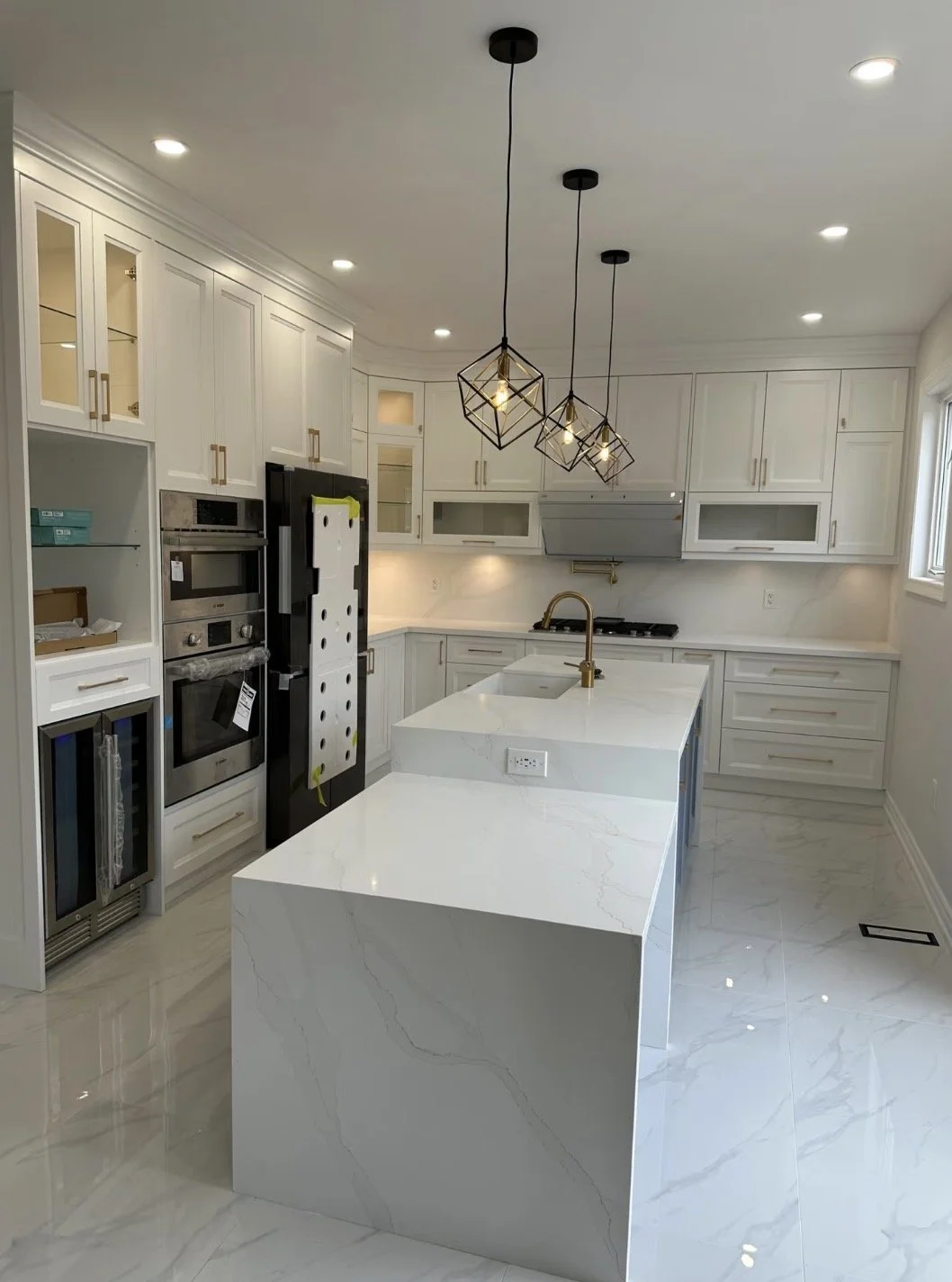 Modern kitchen with white cabinets, marble island, pendant lights, and stainless steel appliances.