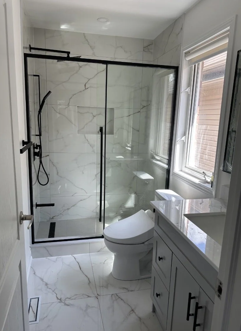 Modern bathroom with a marble shower, white toilet, and a vanity with a white countertop next to a window.