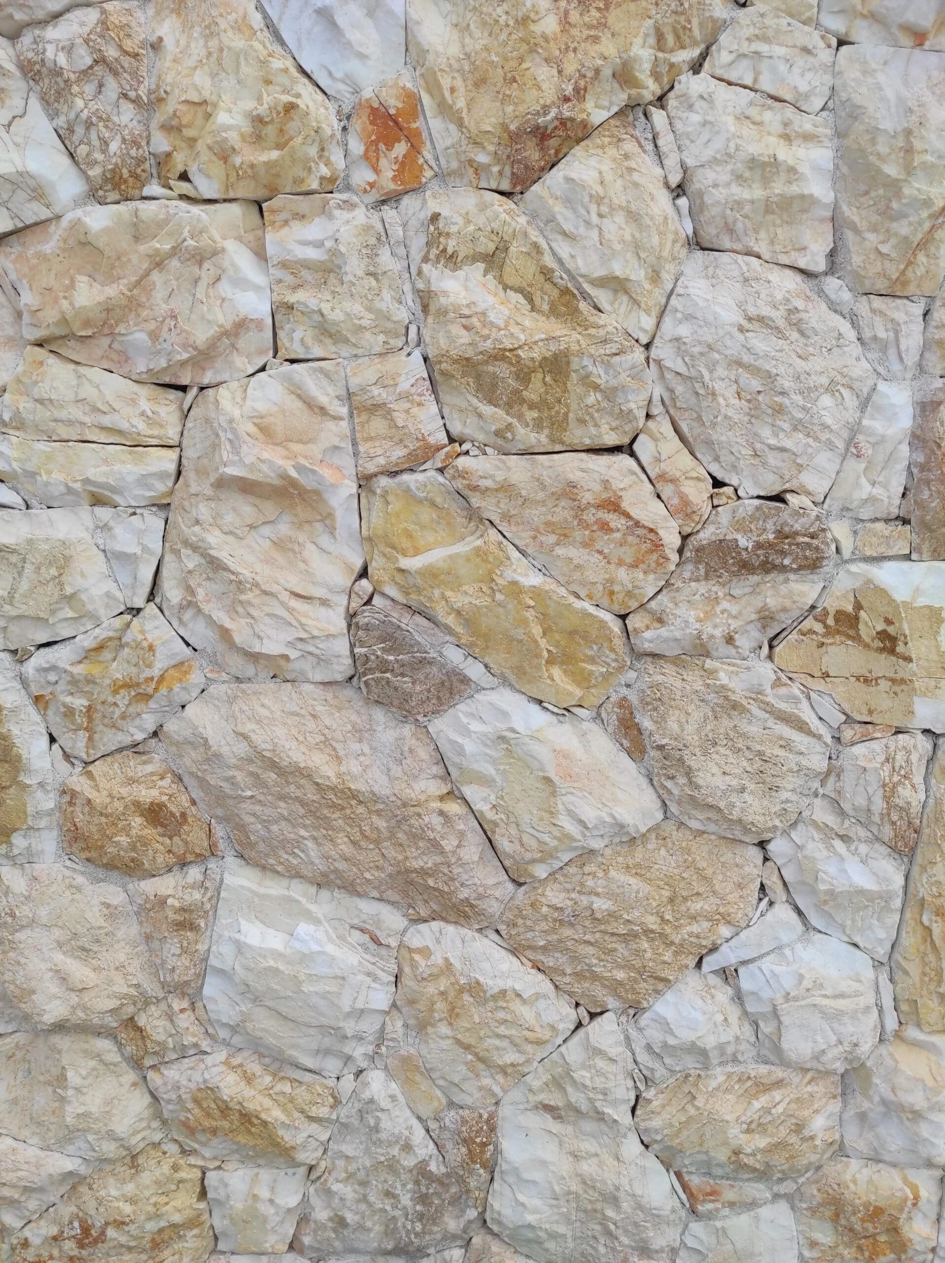Close-up of a stone wall made of irregularly shaped beige and light brown stones.