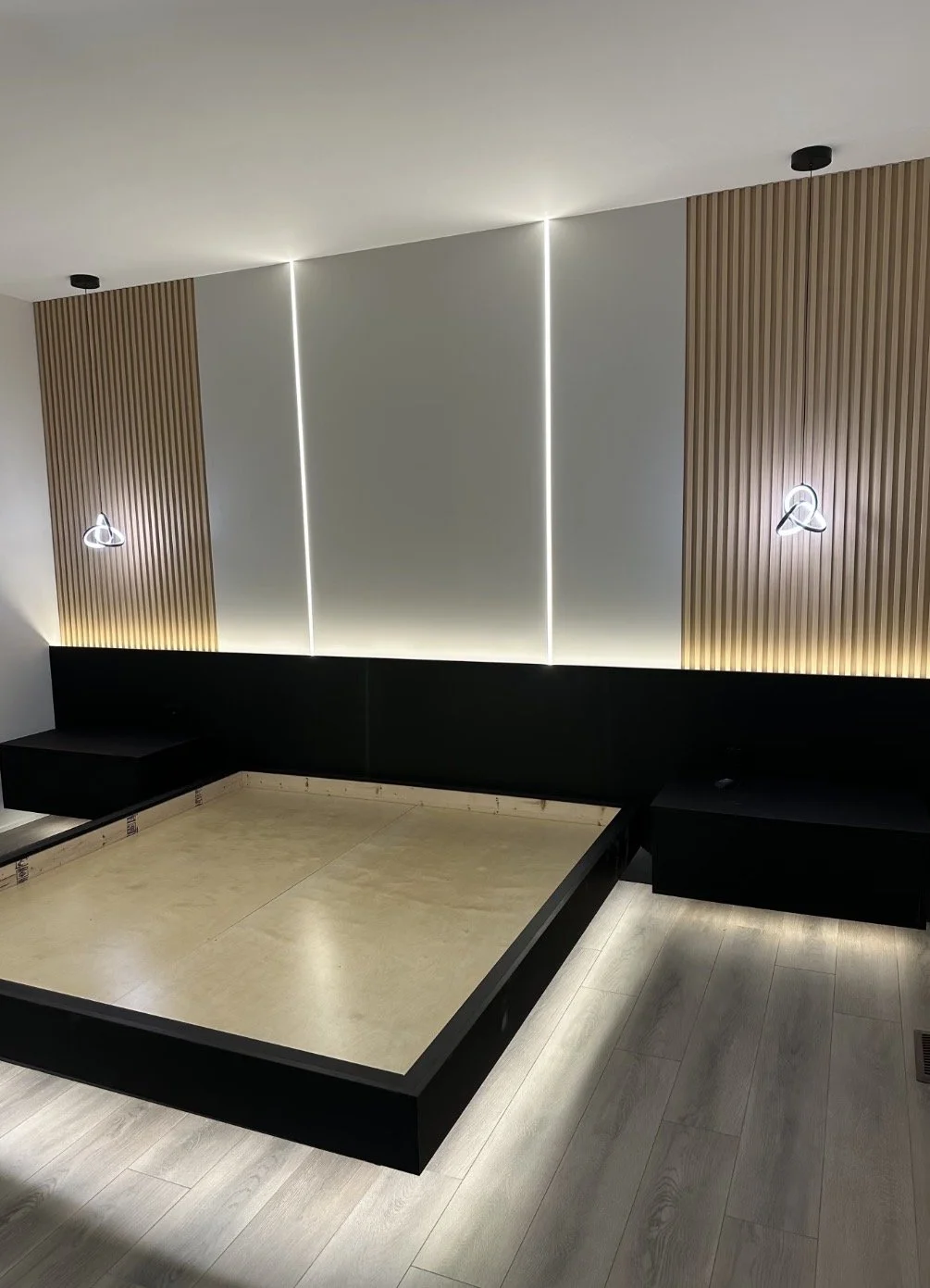 Empty room with a bed frame, modern lighting, and wood paneling on the walls.