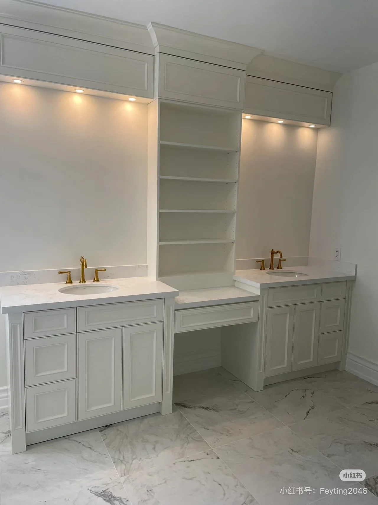 Bathroom vanity with double sinks, white cabinetry, marble countertops, gold faucets, open shelving in the center, recessed lighting above the vanity, and marble tile flooring.