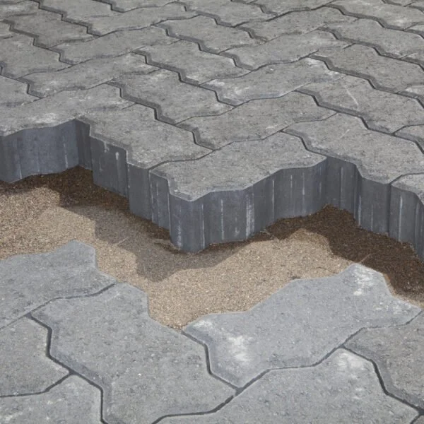 Close-up of broken interlocking paving stones revealing sand and soil underneath.