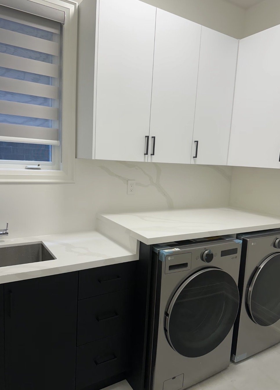Laundry room with white cabinets, a small window with a striped blind, a white countertop, a small sink, and a washer and dryer.