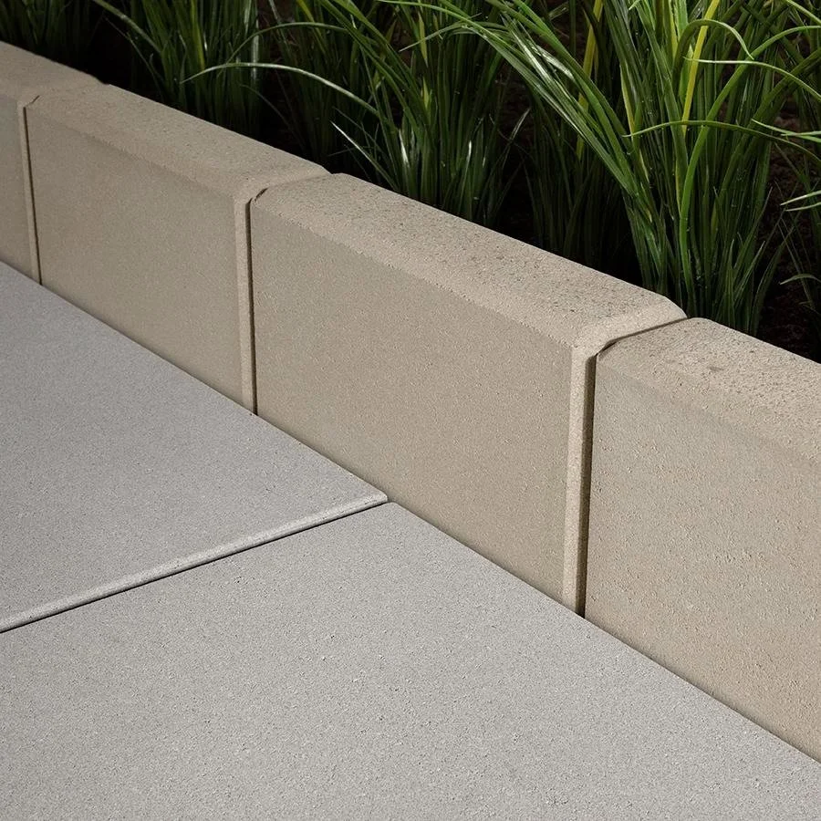 Concrete sidewalk with a beige concrete block wall and green plants in the background.