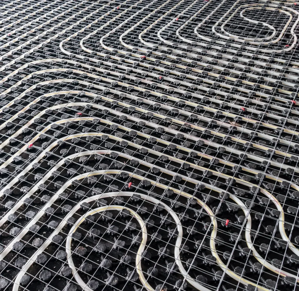 Close-up view of a hydronic heating system with an intricate network of pipes, valves, and a metal grid for support, used in radiant floor heating installations.