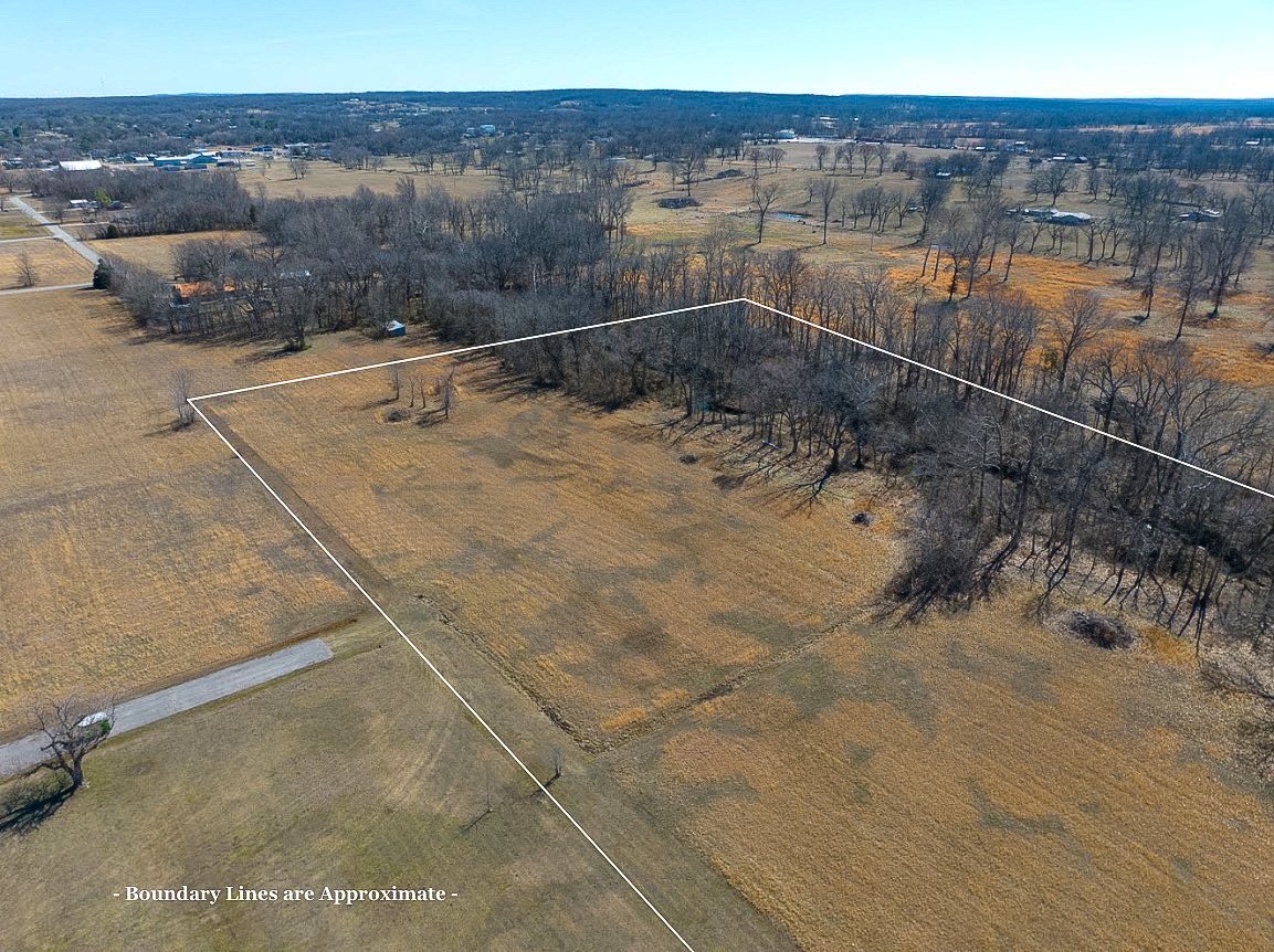 Aerial view of a large open farm land with a boundary line marked, some trees, fields, and a few structures in the background, on a clear day.