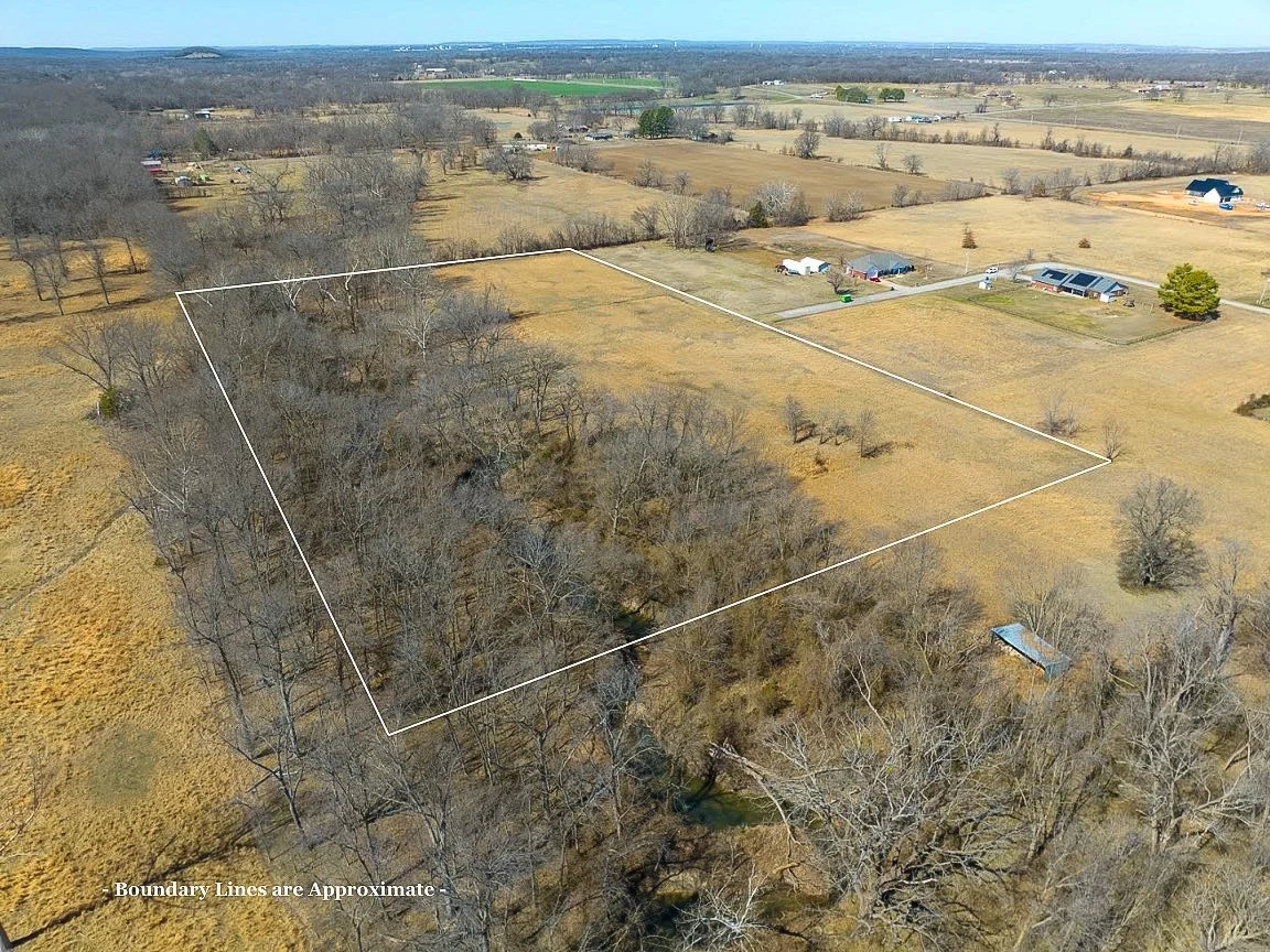 Aerial view of a large, mostly cleared property with a border outline, surrounded by trees and some neighboring houses and open fields.