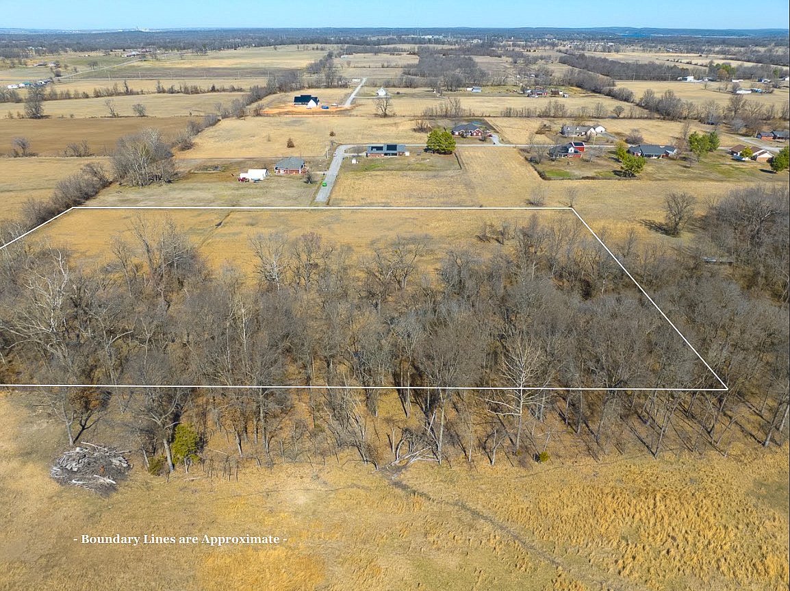 Aerial view of a rural area showing open fields, scattered houses, and trees, with white boundary lines marking a specific property plot.