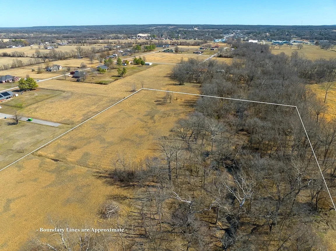 Aerial view of a rural area showing fields, houses, and a wooded area with boundary lines marked around the land.