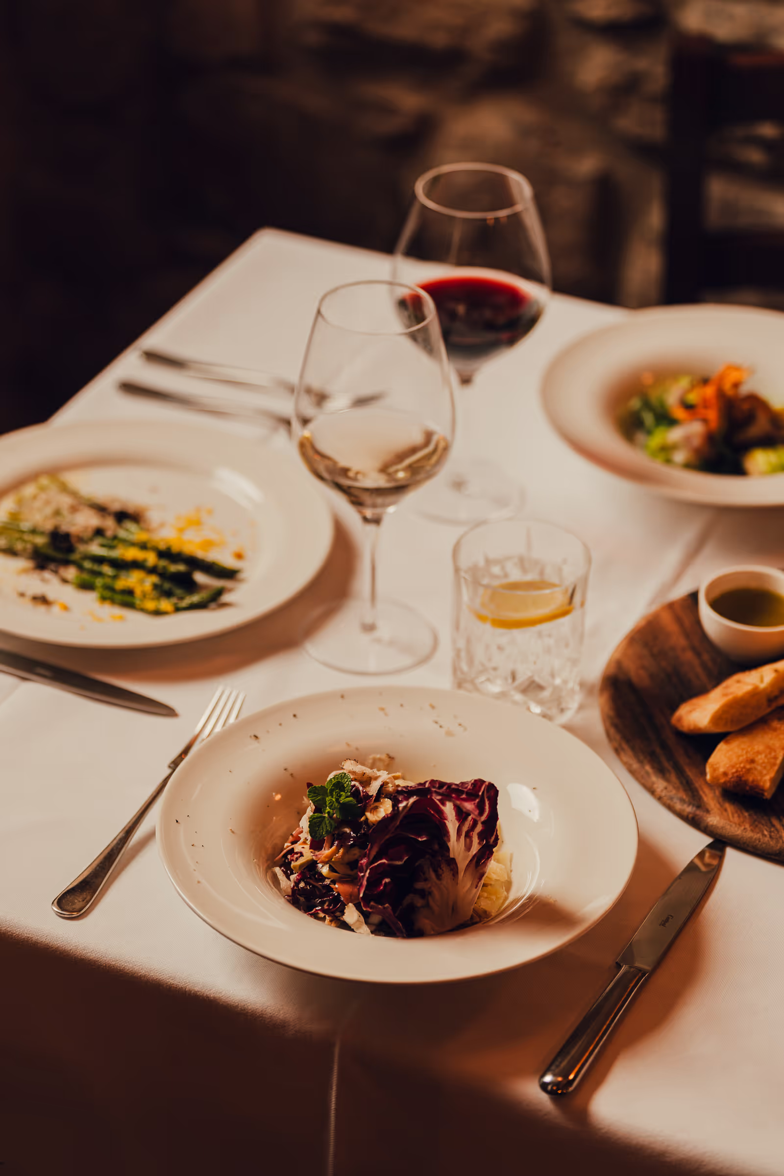 A dinner table with plates of salad, glasses of red and white wine, bread, and a glass of water, set for a meal.